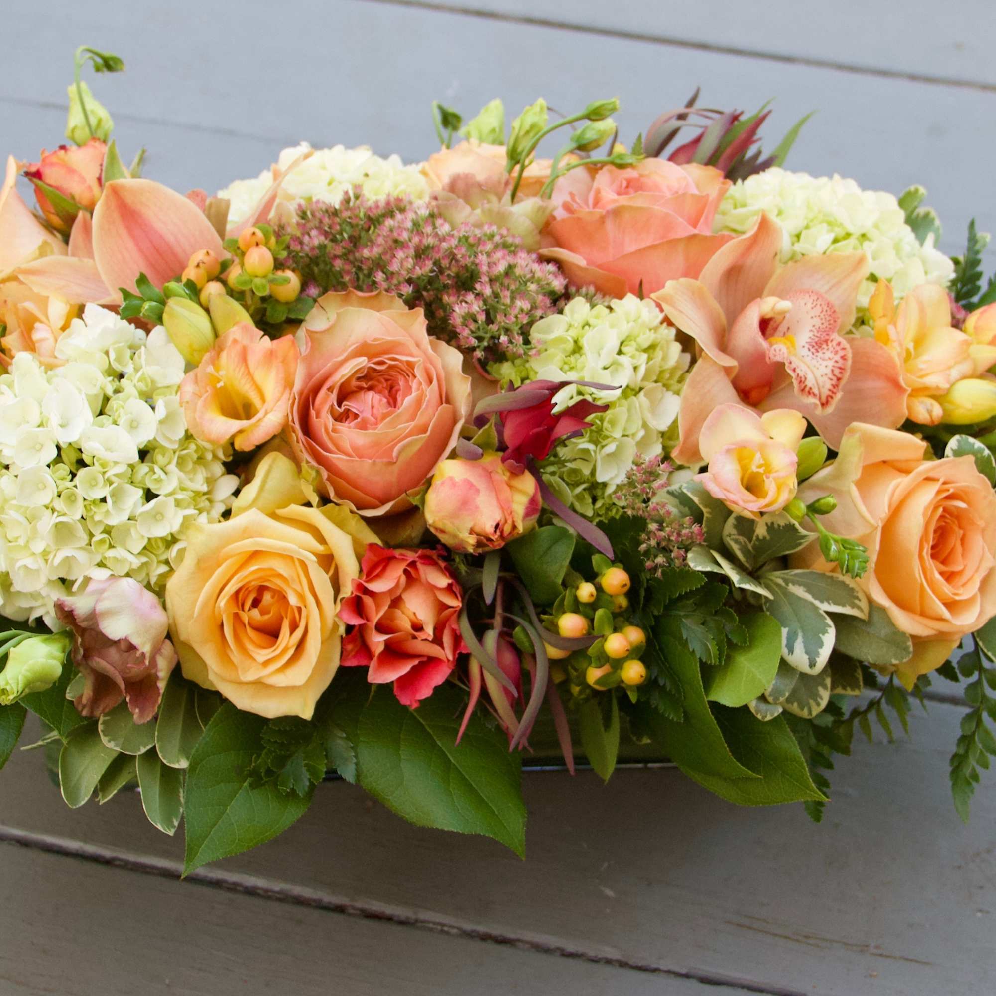 Low floral arrangement with peach roses and white hydrangeas on a gray surface.