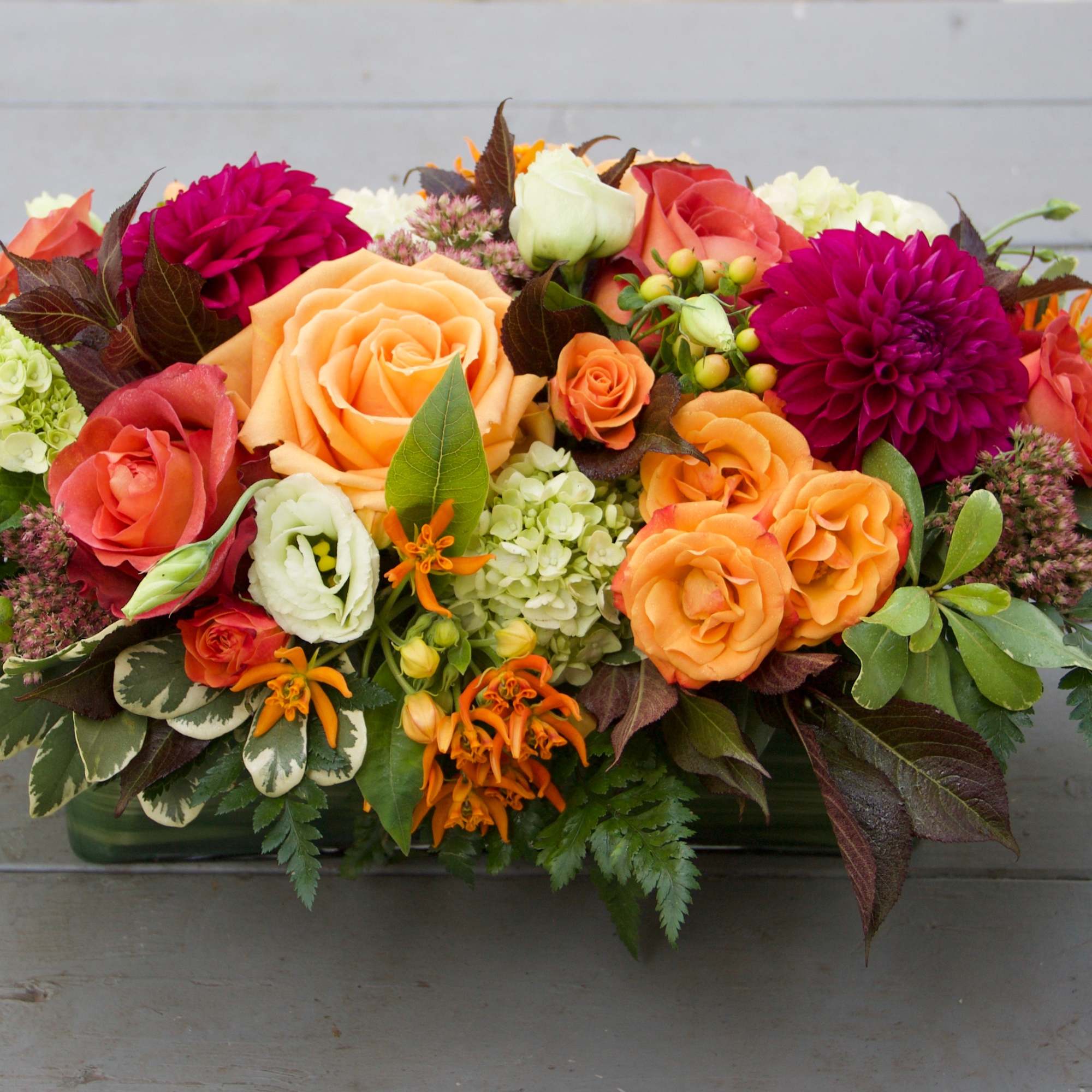 Mixed bouquet of orange, pink, and white flowers in a low rectangular container