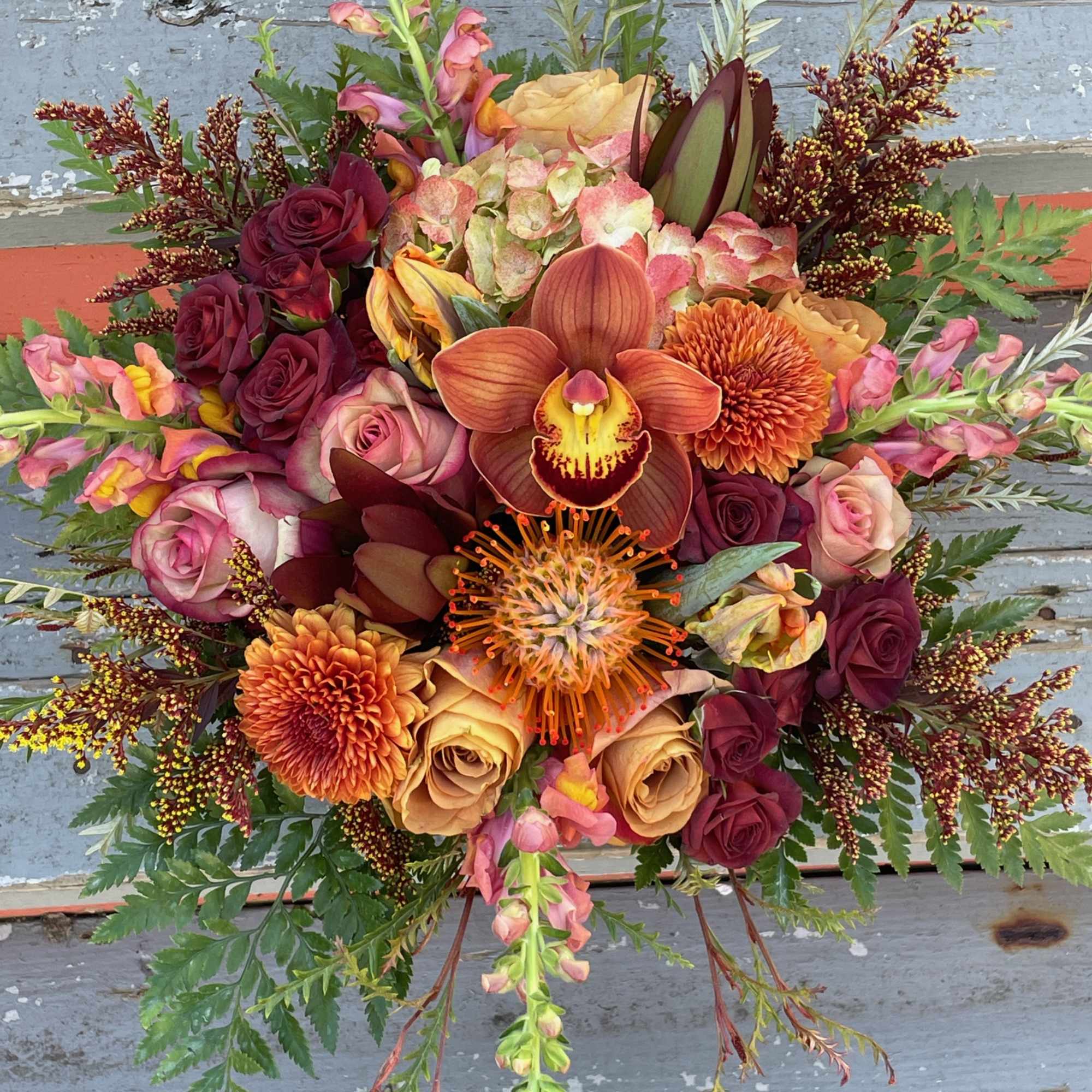 Mixed bouquet with roses, orchids, and orange mums in warm fall colors