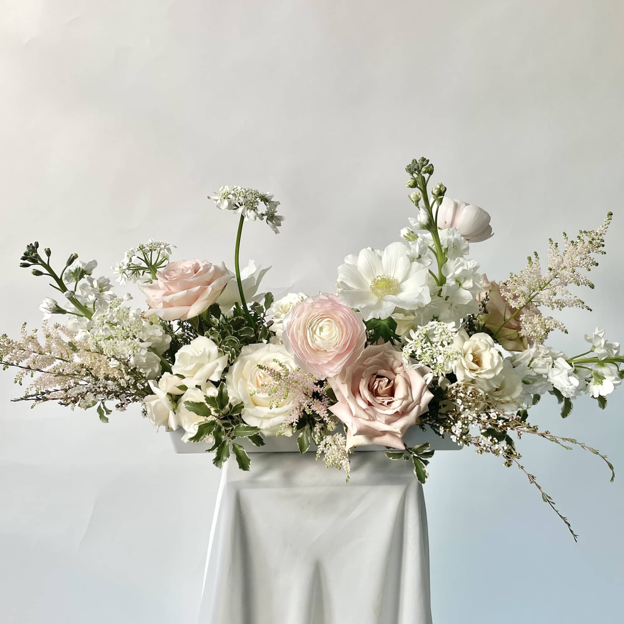 Pastel rose and white floral arrangement in a white rectangular vase