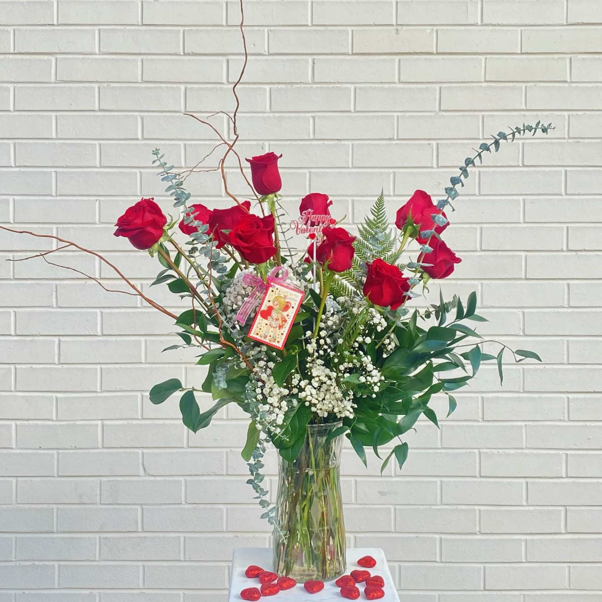 Tall vase arrangement of red roses with greenery and baby's breath