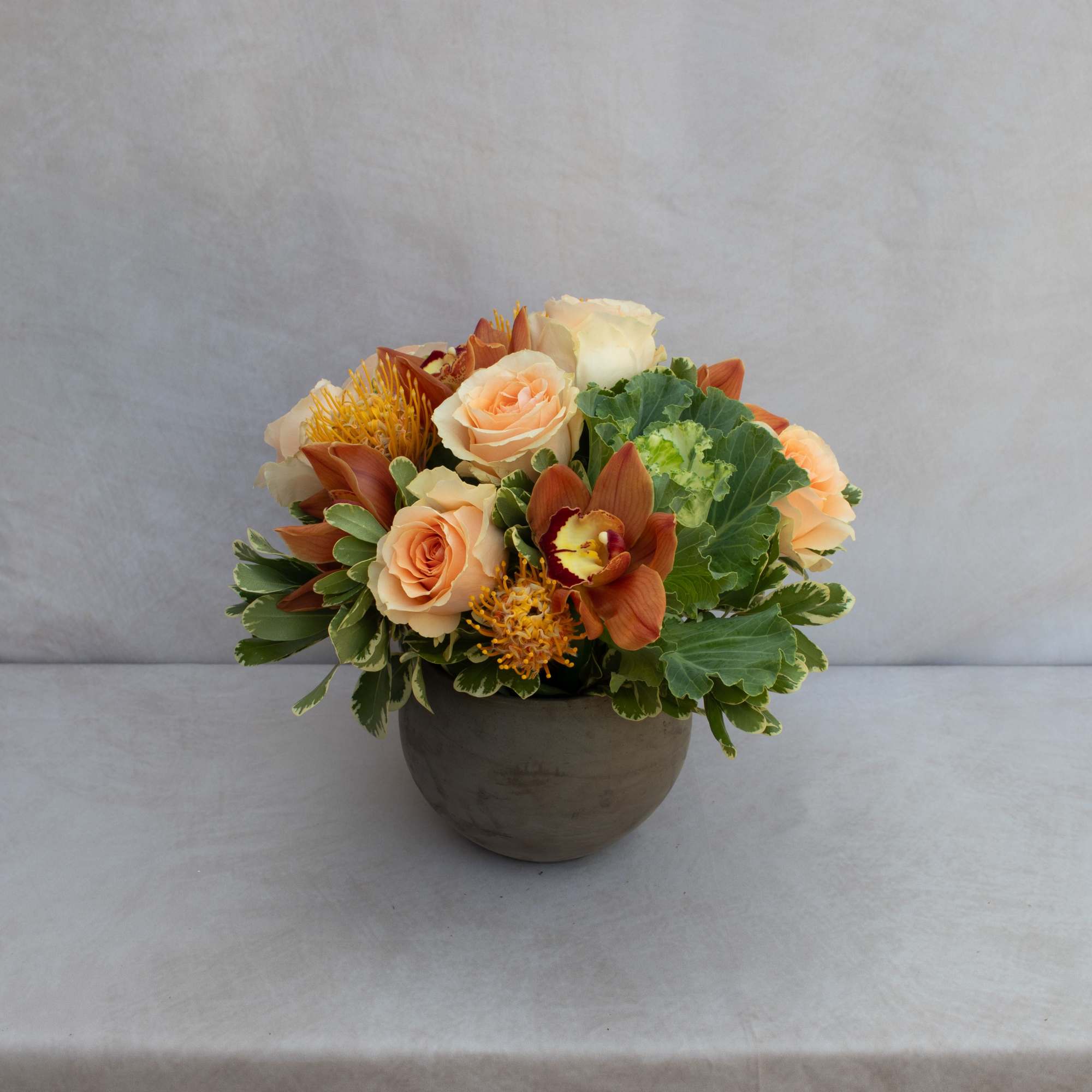 Peach roses and orange orchids arranged in a round vase