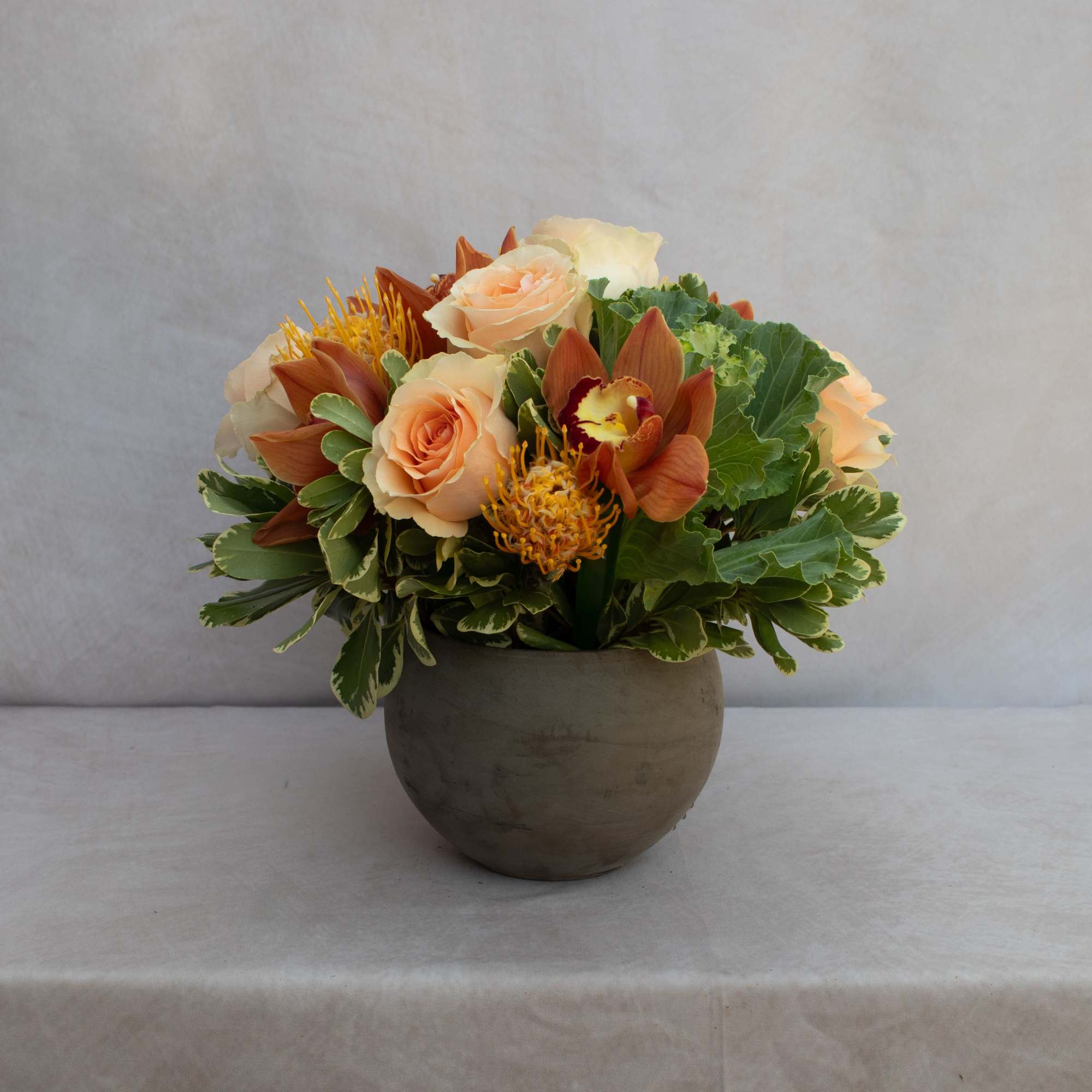 Peach roses and orange orchids arranged in a round gray vase