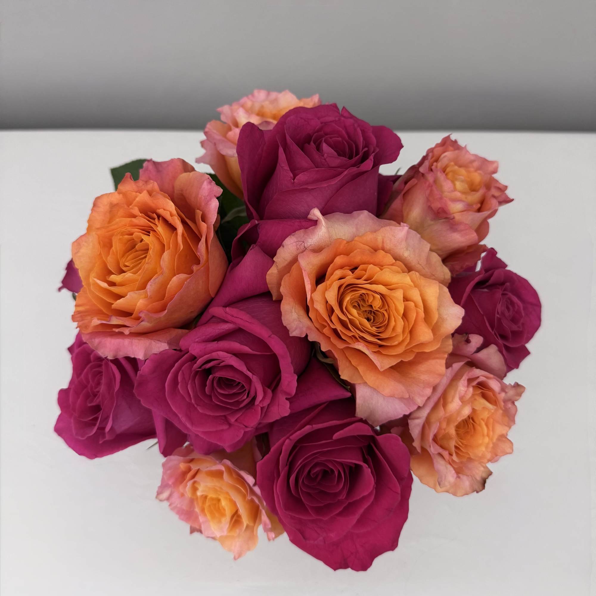 Bouquet of orange and magenta roses on a white surface