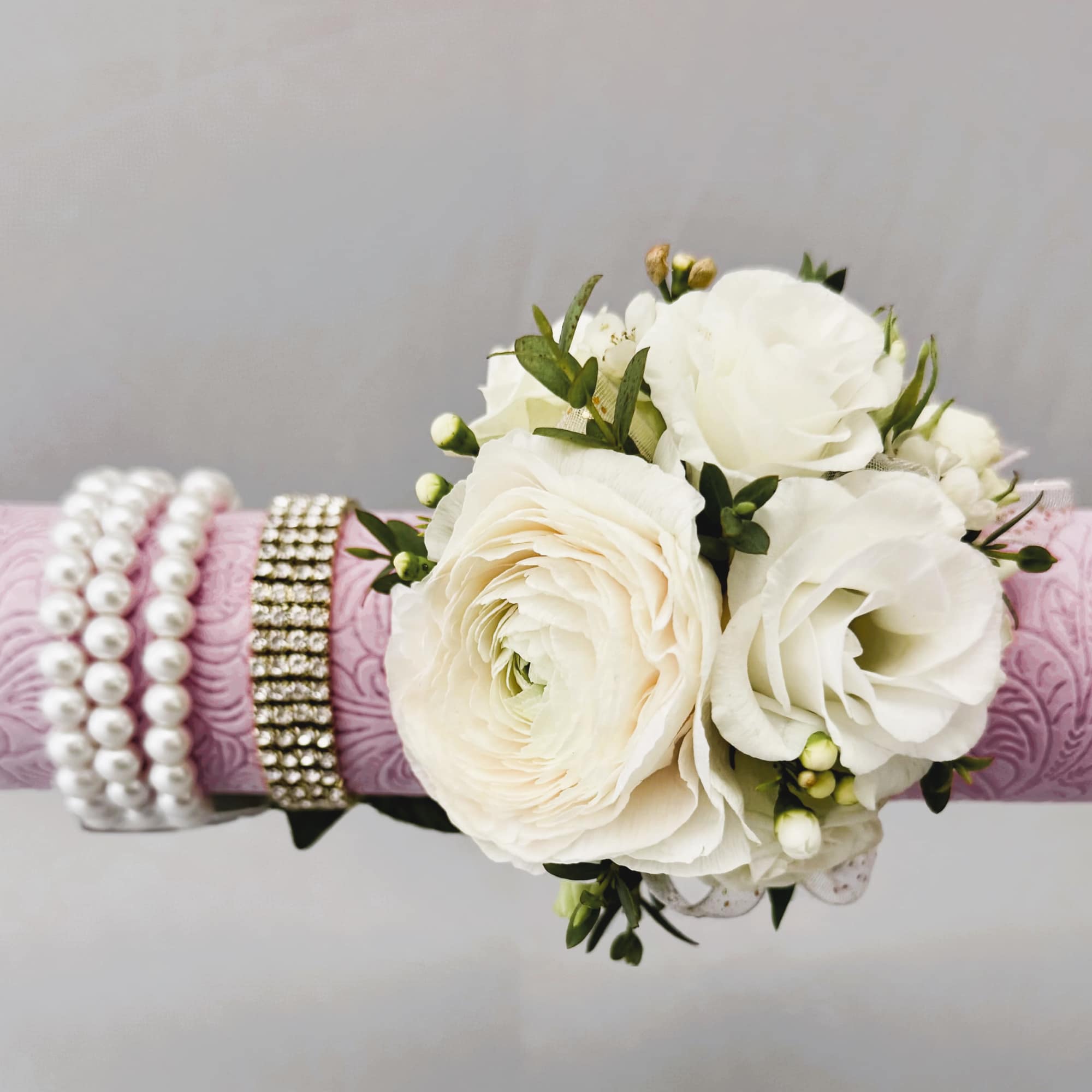 White floral wrist corsage on a pink patterned band with pearl and rhinestone bracelets