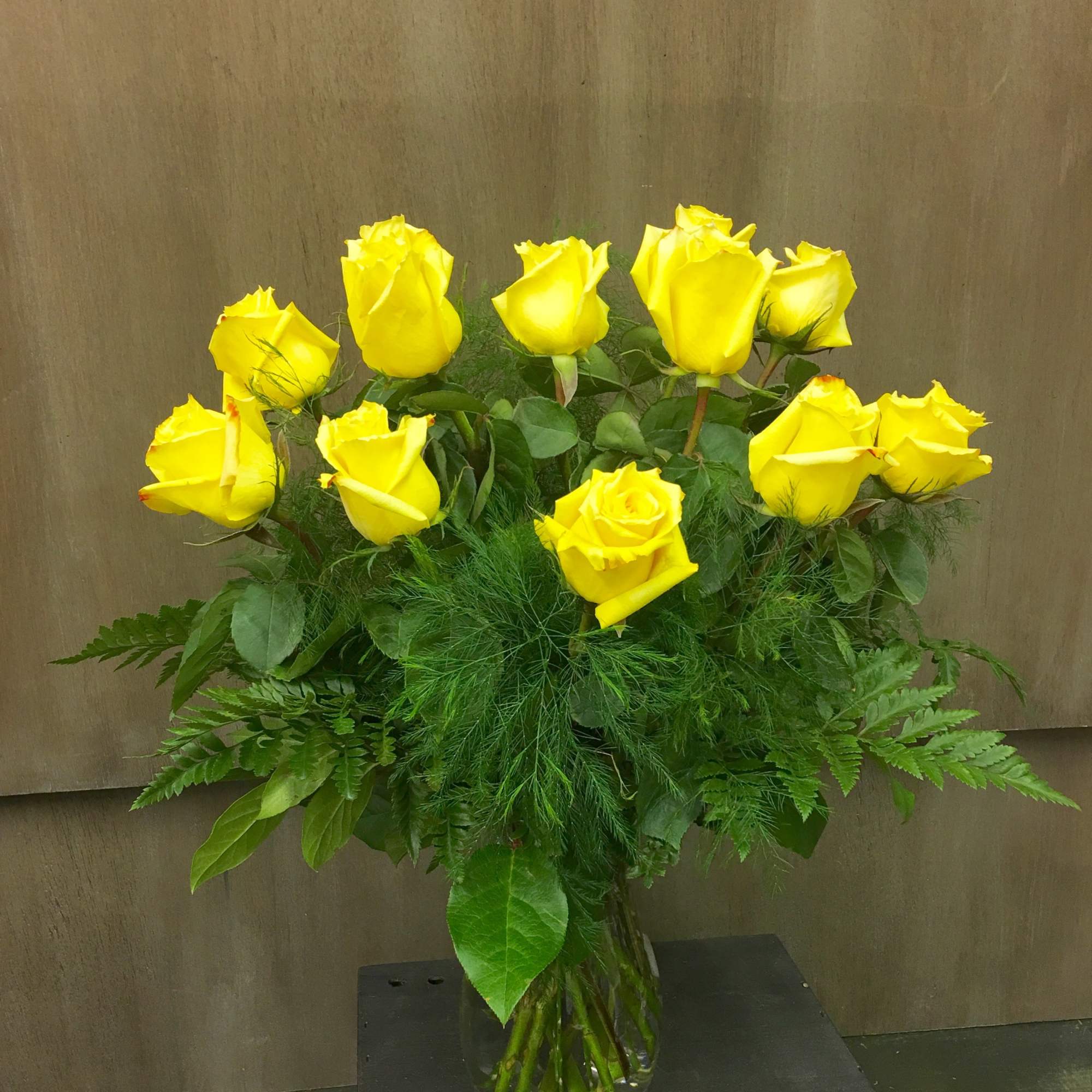 Yellow roses arranged in a clear glass vase with lush greenery