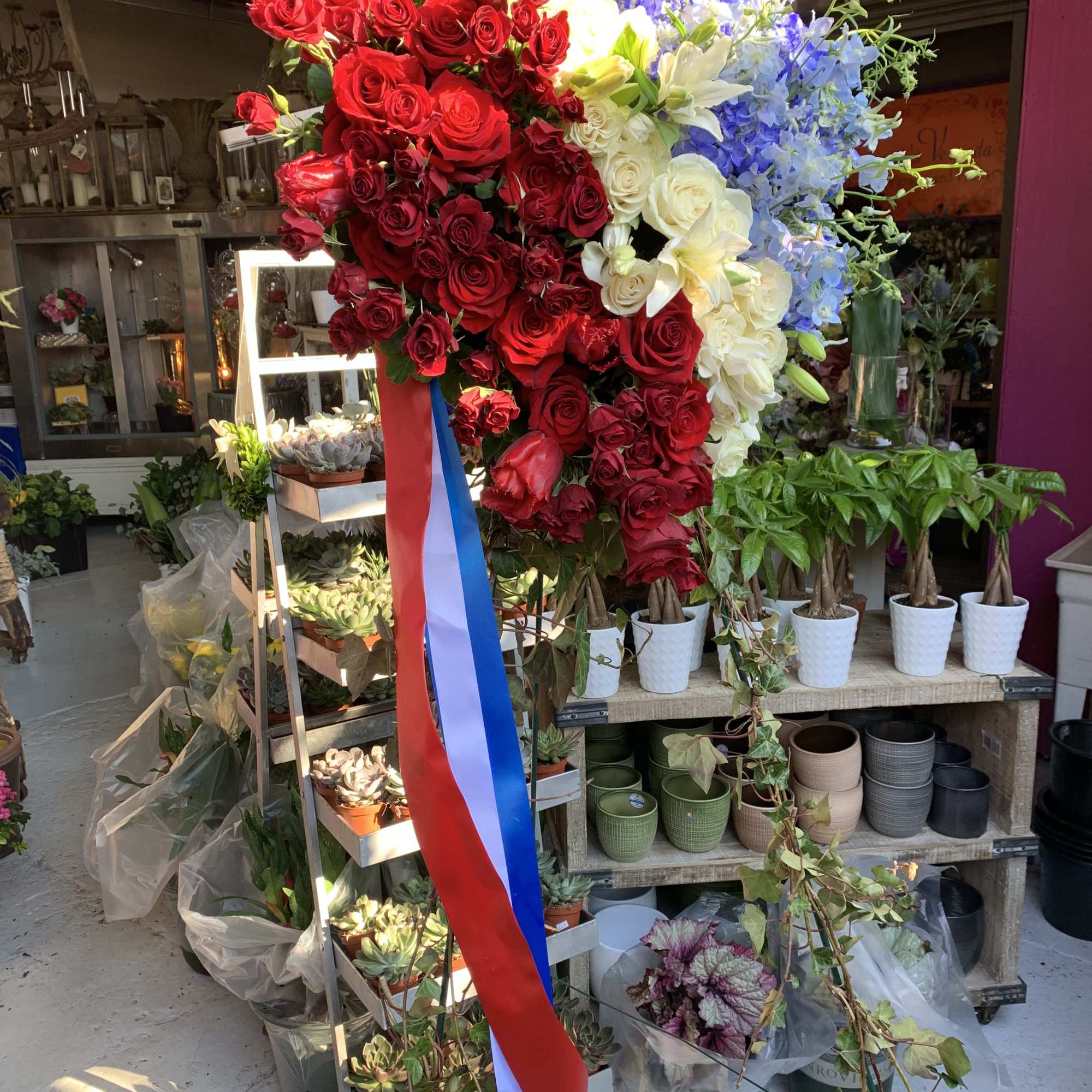 Large standing floral heart of red, white, and blue flowers with ribbon streamers