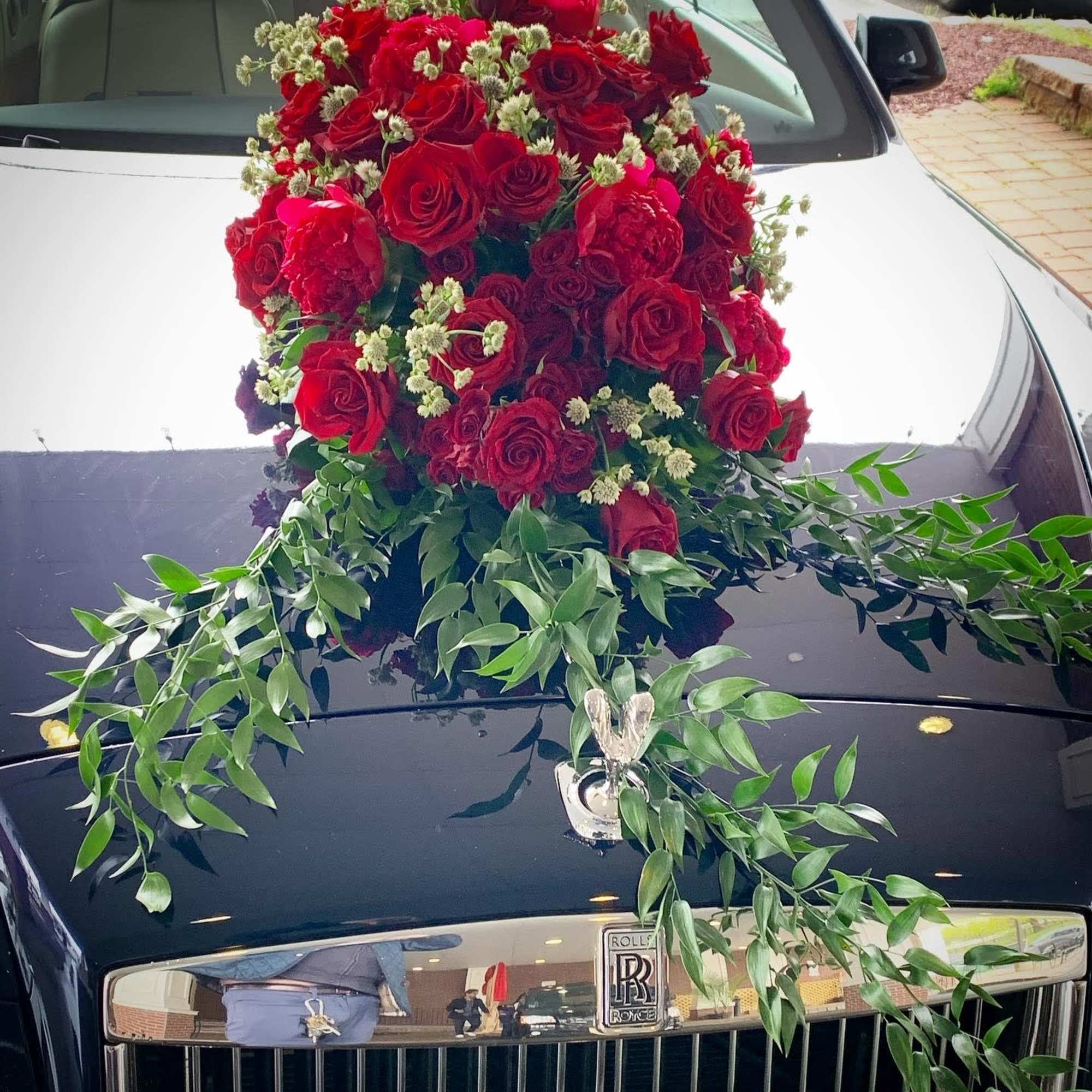 Large red rose arrangement draped over the hood of a black Rolls-Royce