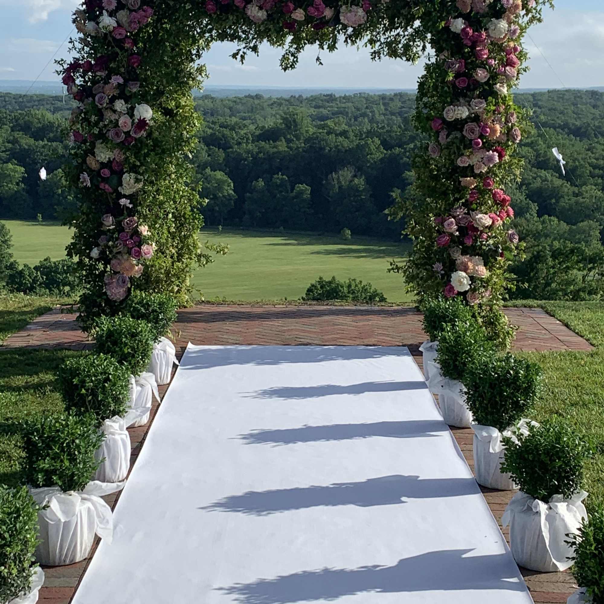 Floral wedding arch with pink and white roses over a white aisle runner