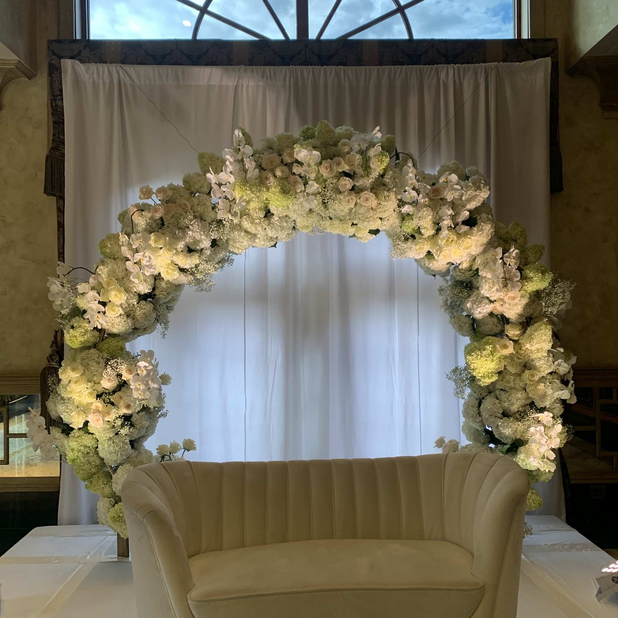 Large floral arch with white and pale green blooms behind a beige loveseat