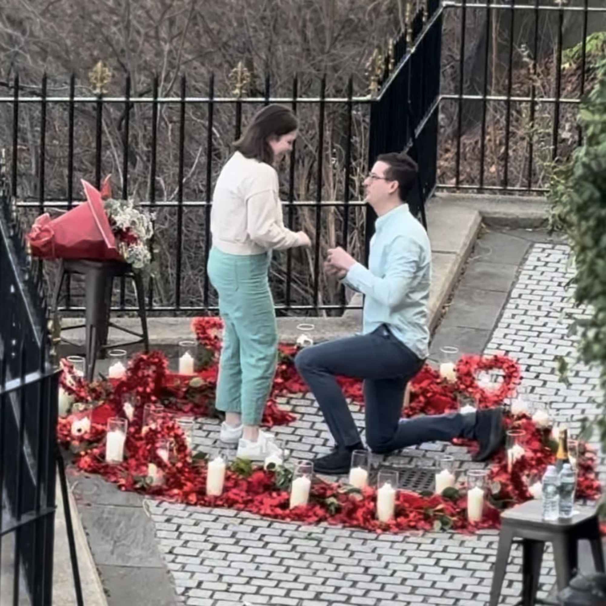 Couple on a candlelit path surrounded by red flower petals and a bouquet on a stool.