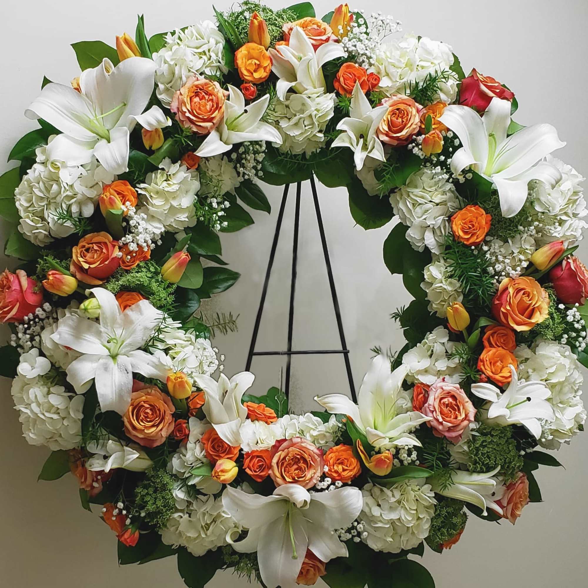 Large floral wreath with white lilies, orange roses, and white hydrangeas on an easel