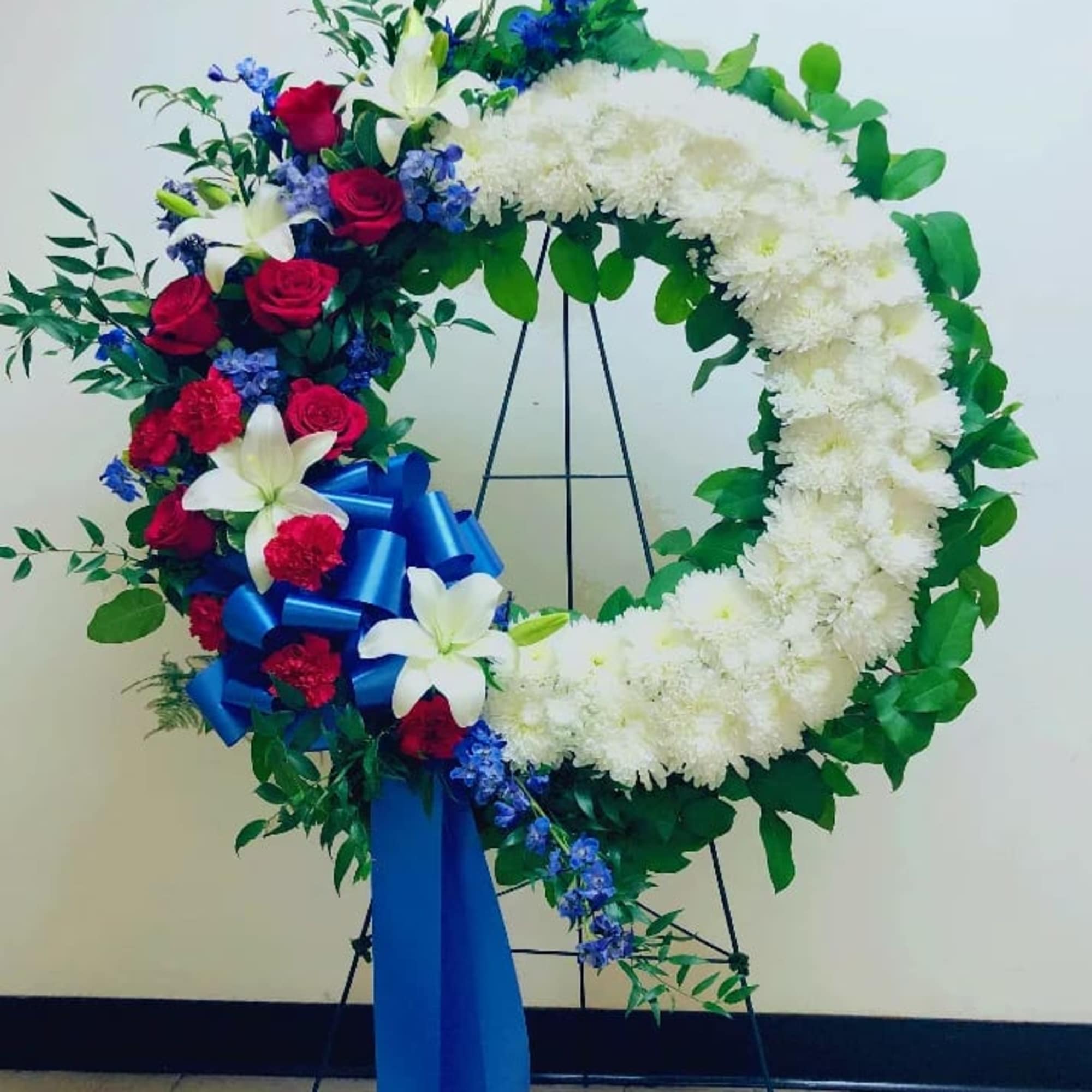 Heart-shaped floral wreath with white and red flowers and a blue ribbon