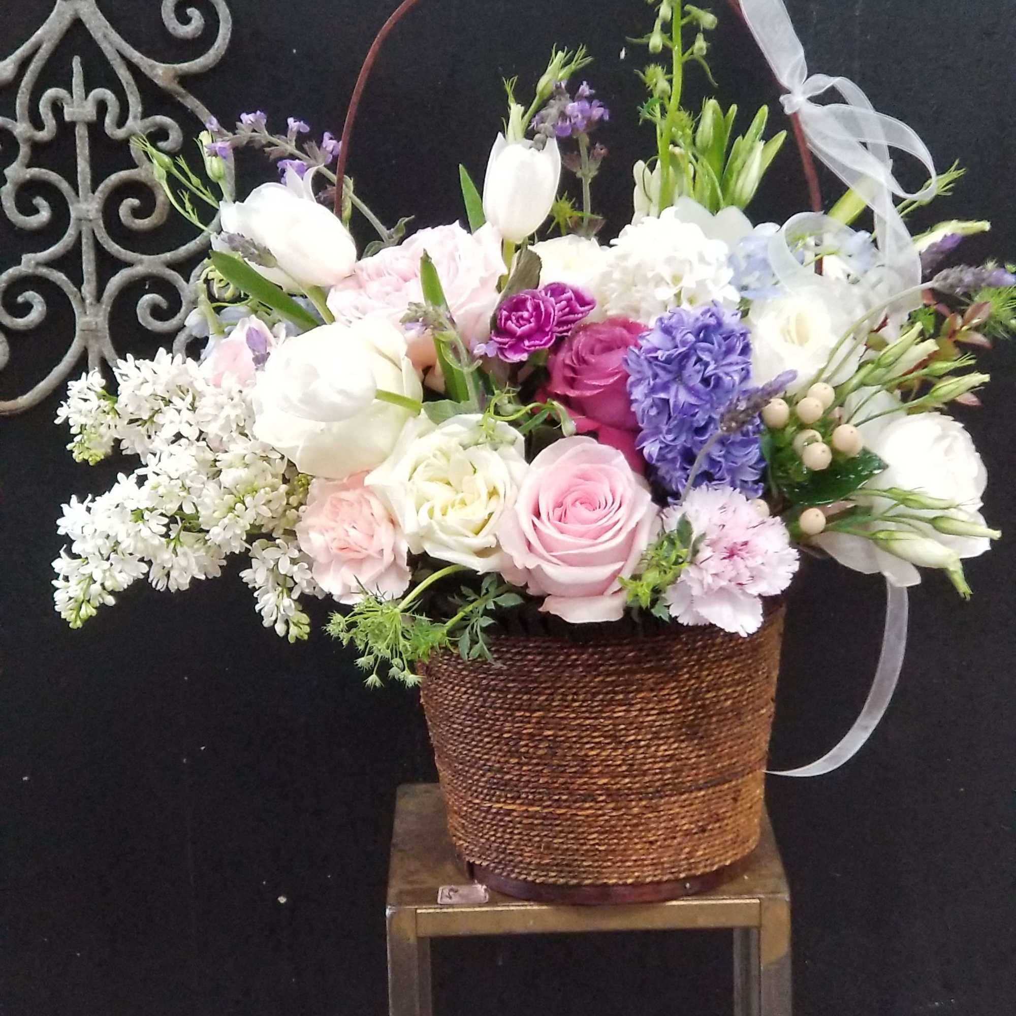 Mixed pastel flower arrangement in a woven basket on a stand
