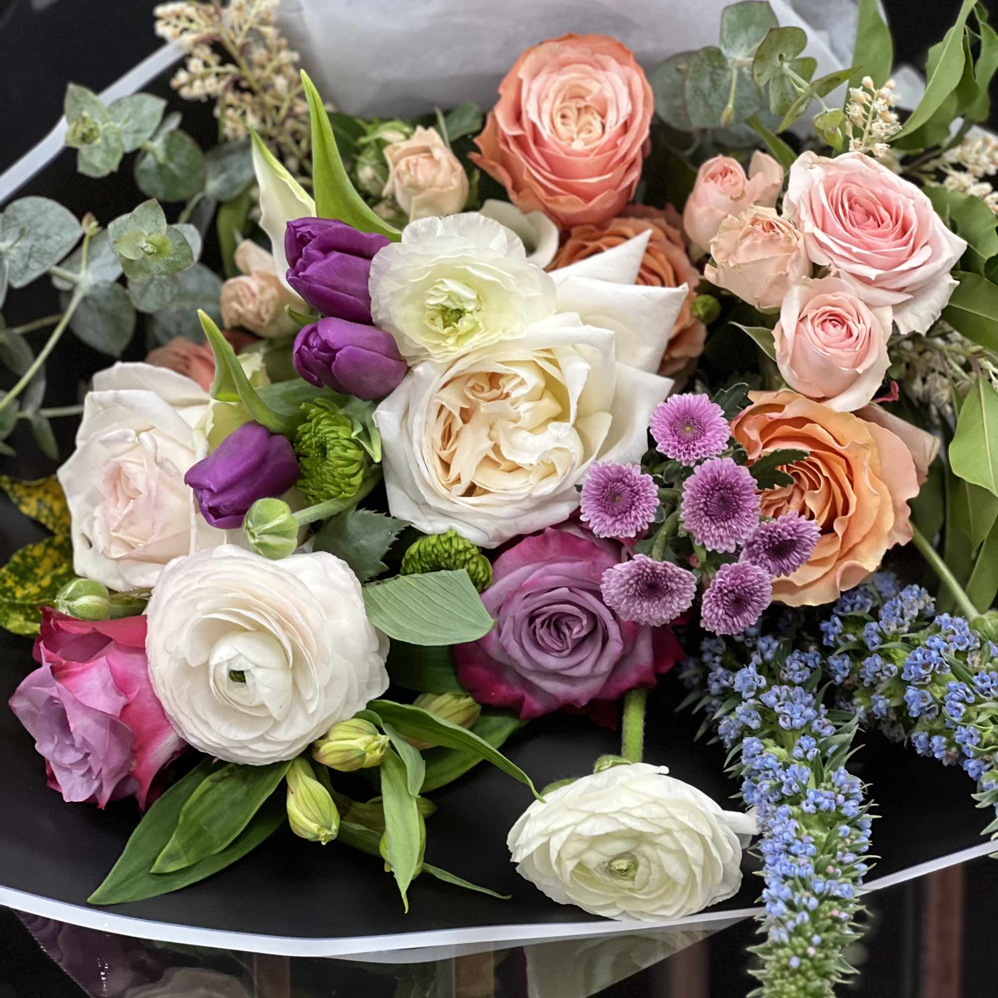 Mixed bouquet of roses, tulips, and purple accent flowers wrapped in black paper