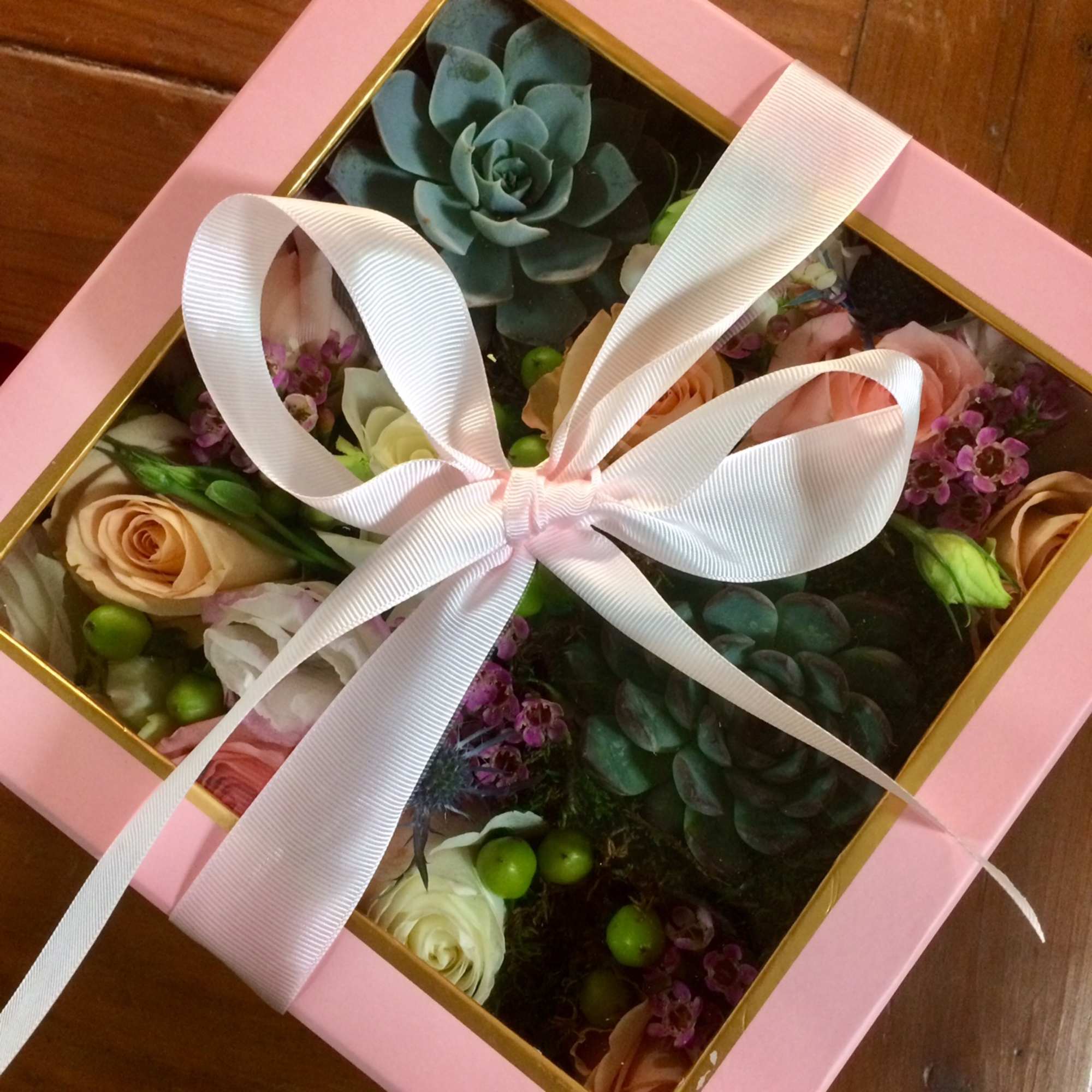 Pink gift box with roses, succulents, and a white ribbon bow