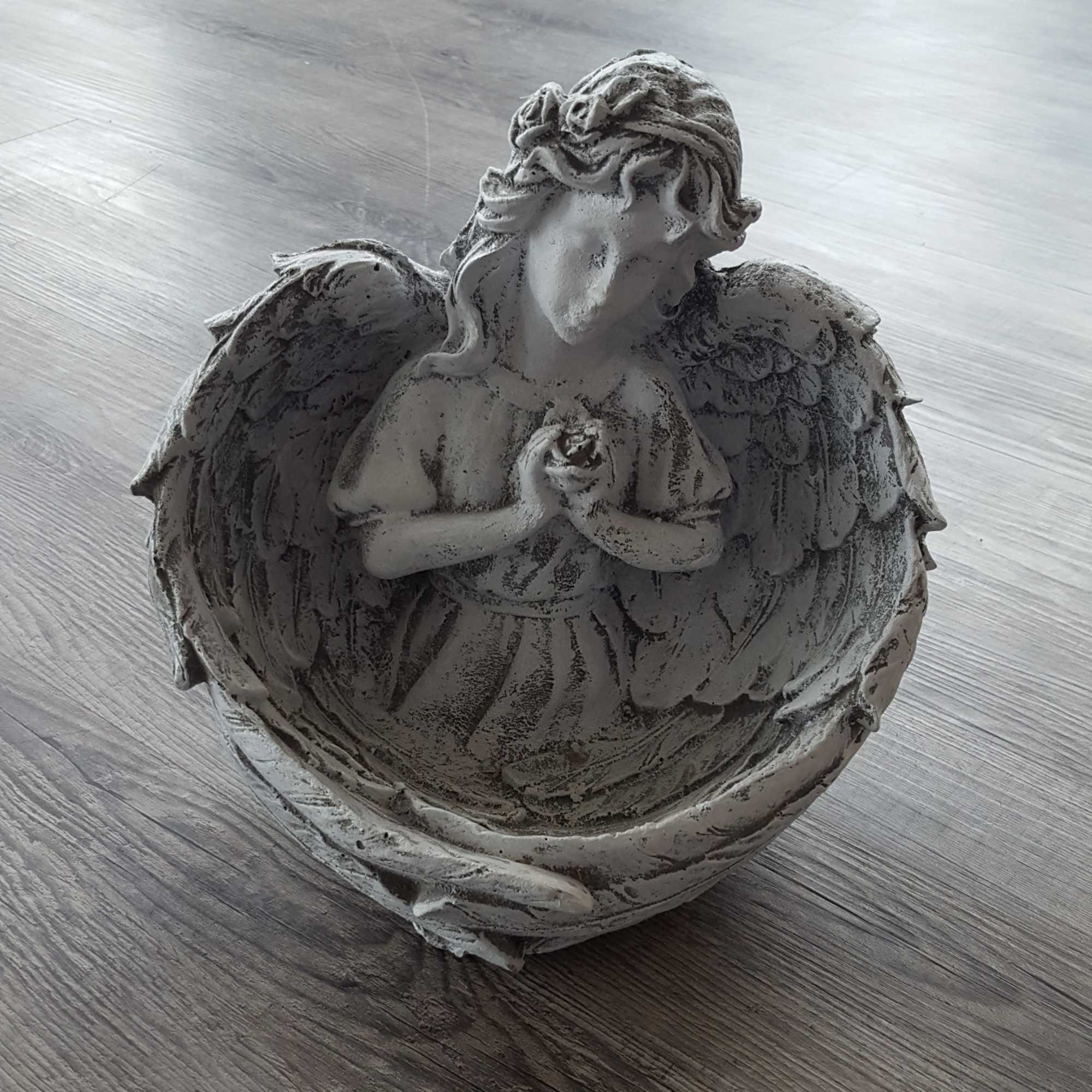 Gray angel figurine with folded hands inside a shell-shaped holder