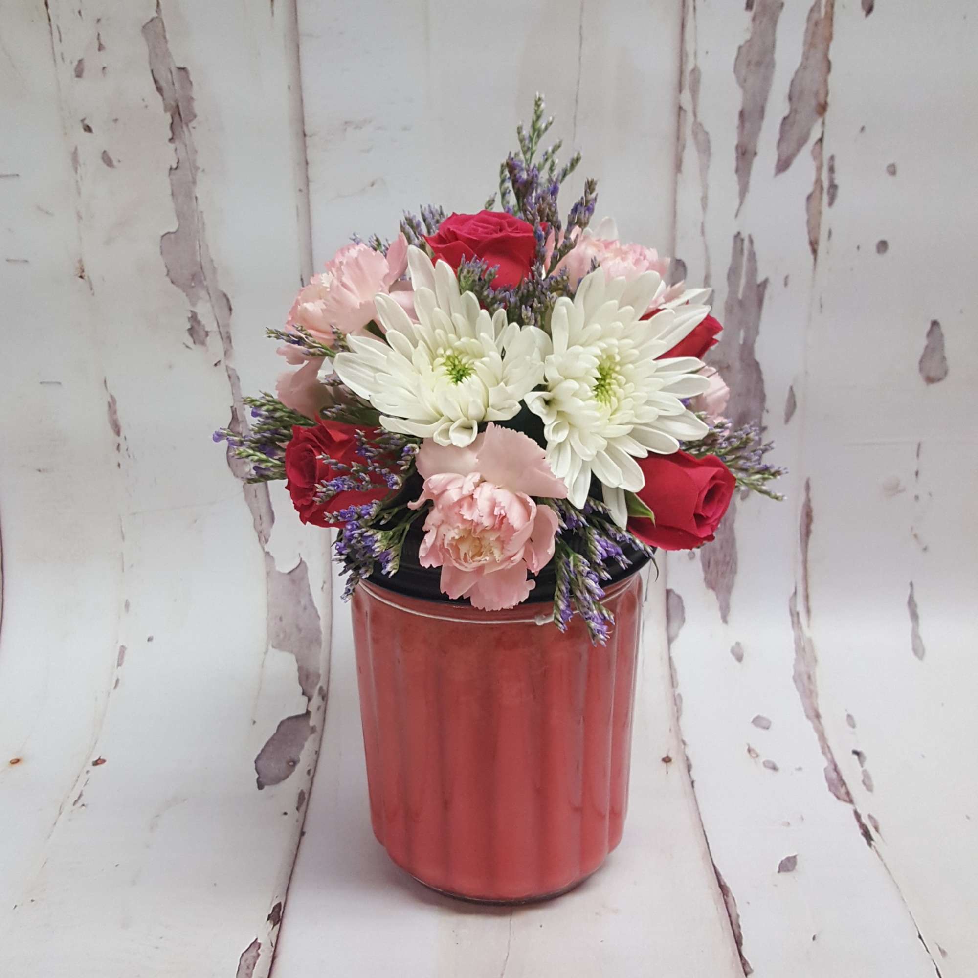Bouquet of red roses, white daisies, and pink carnations in a red vase