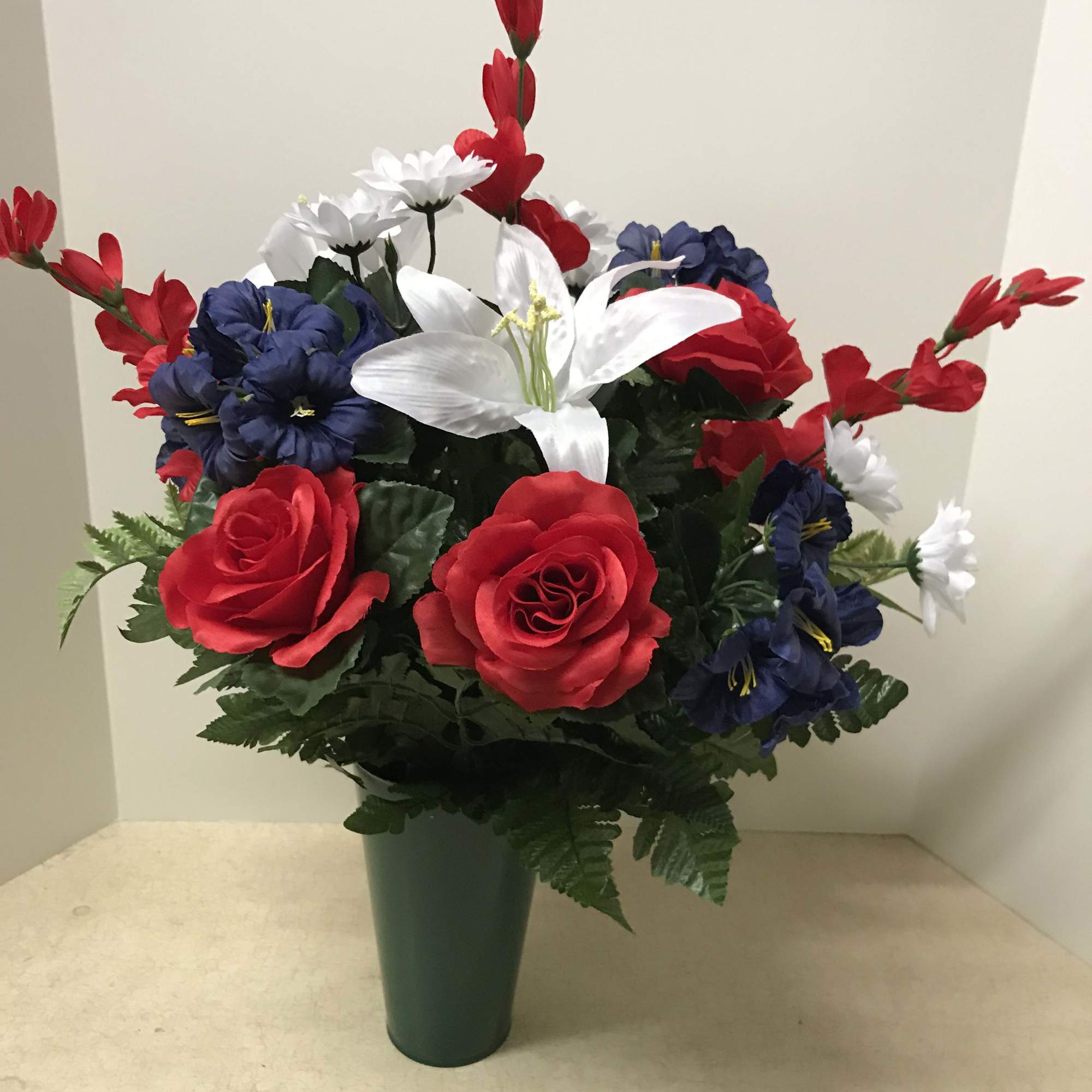 Artificial red, white, and blue flowers arranged in a green vase