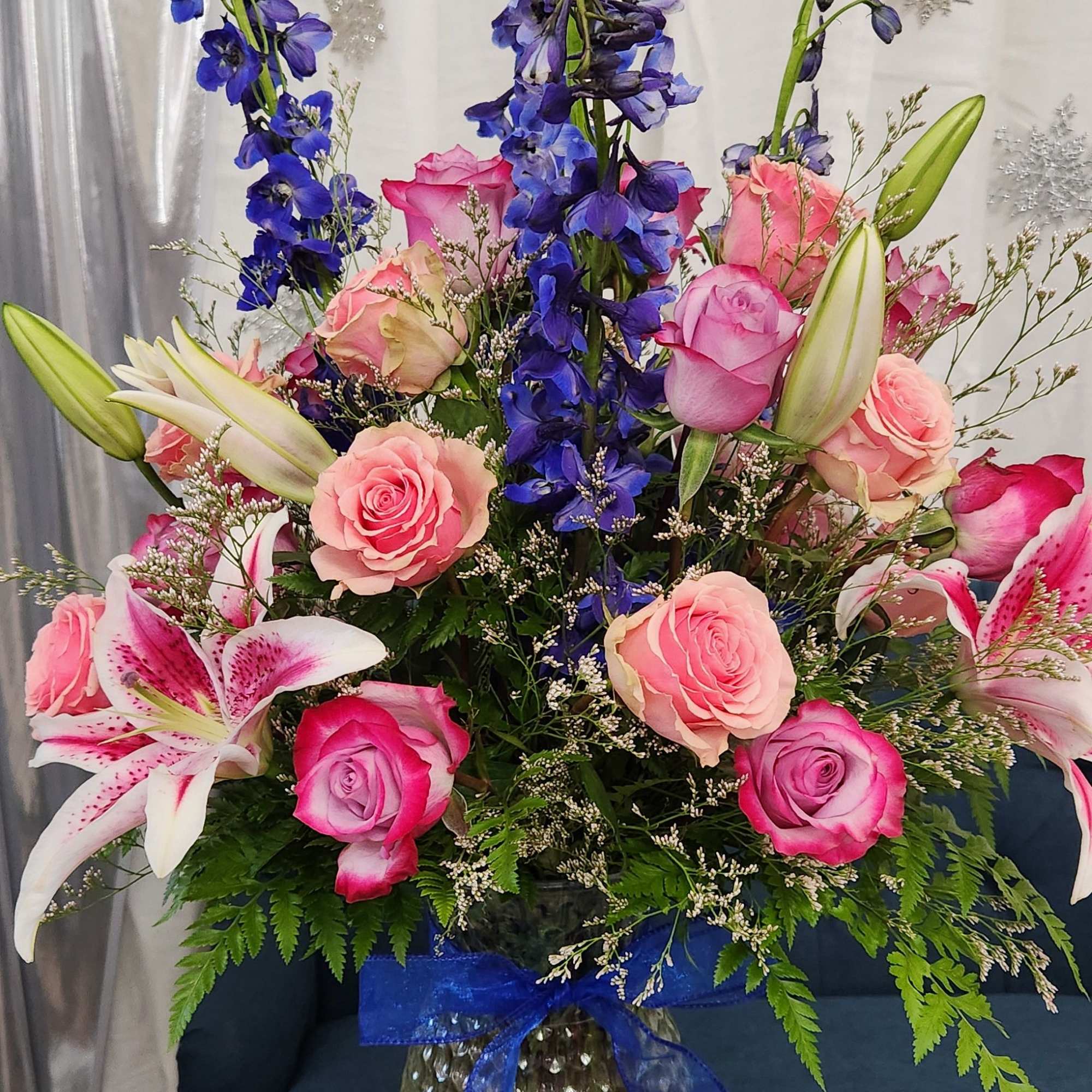 Tall bouquet of pink roses, lilies, and blue delphinium in a glass vase