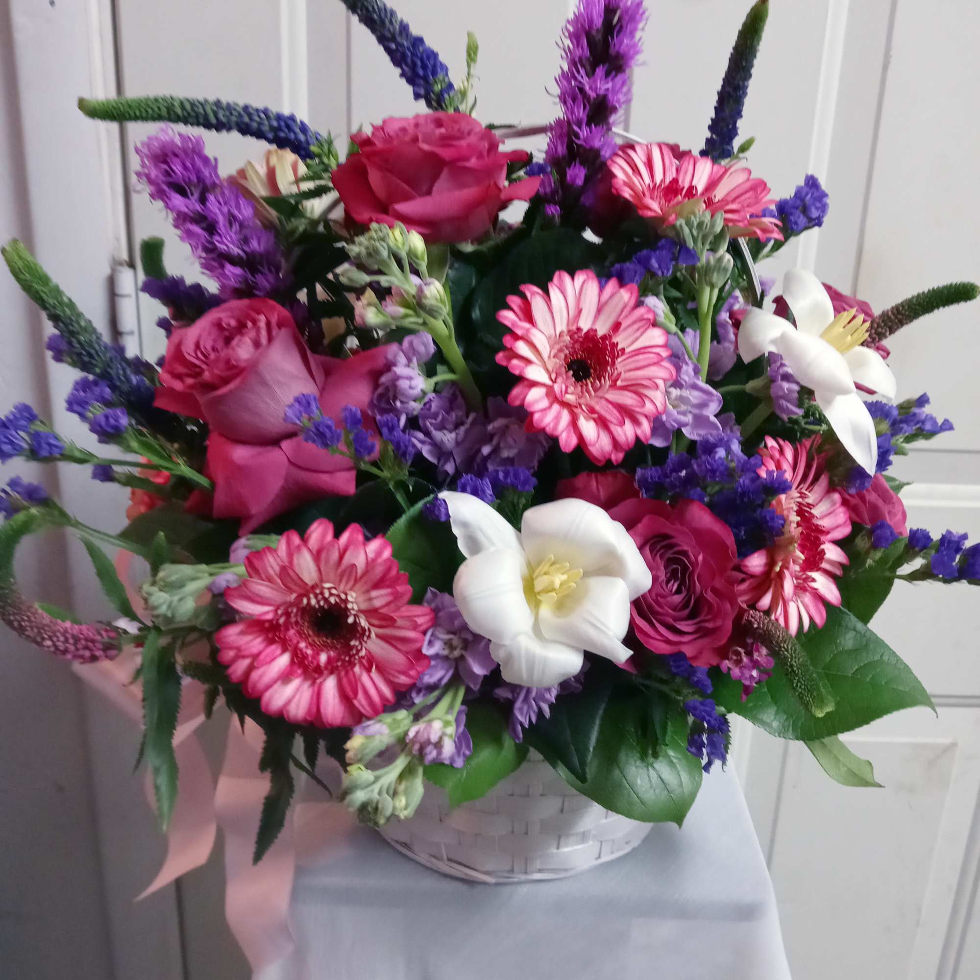Pink roses and gerbera daisies in a white basket with purple accents