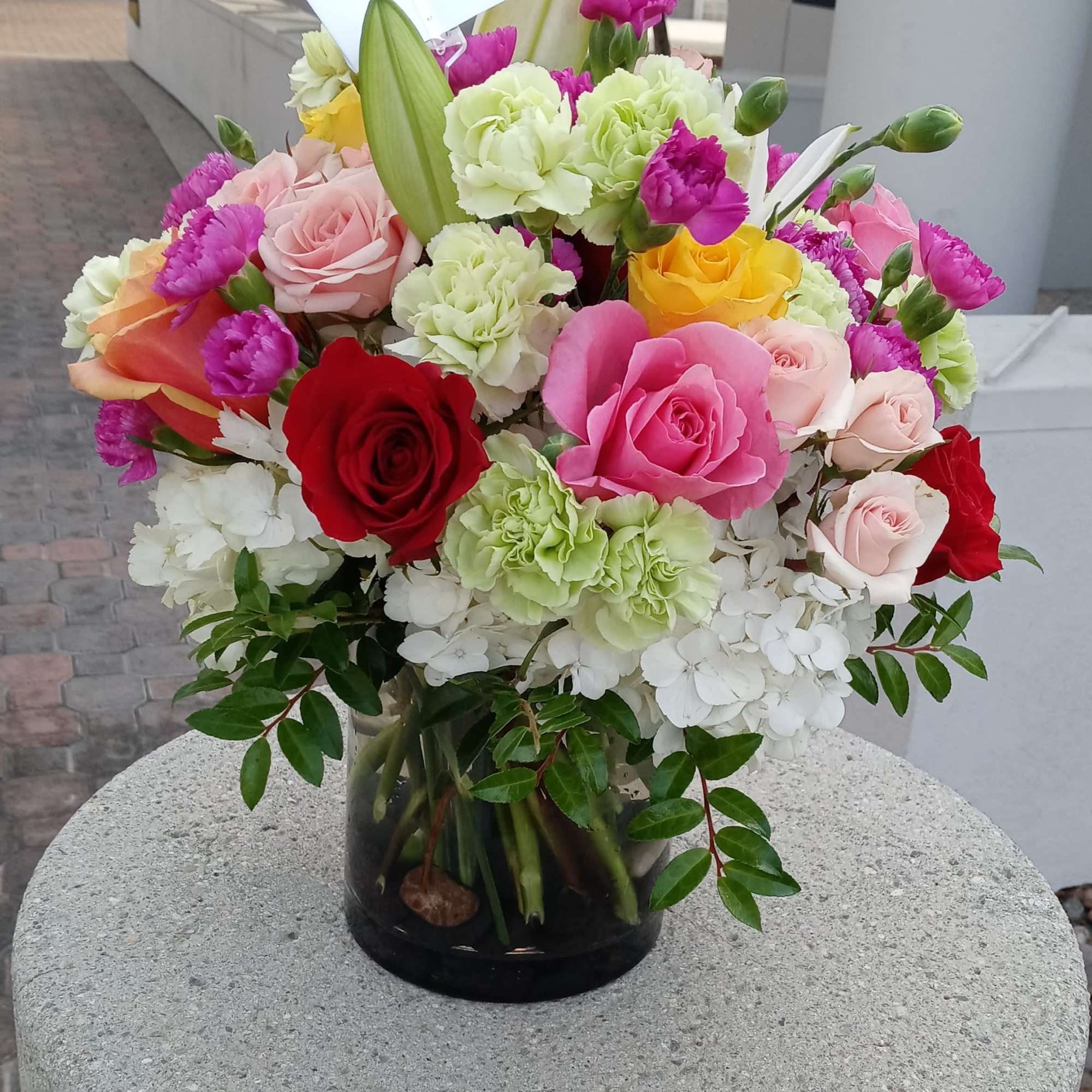 Mixed bouquet of roses, carnations, and hydrangeas in a glass vase