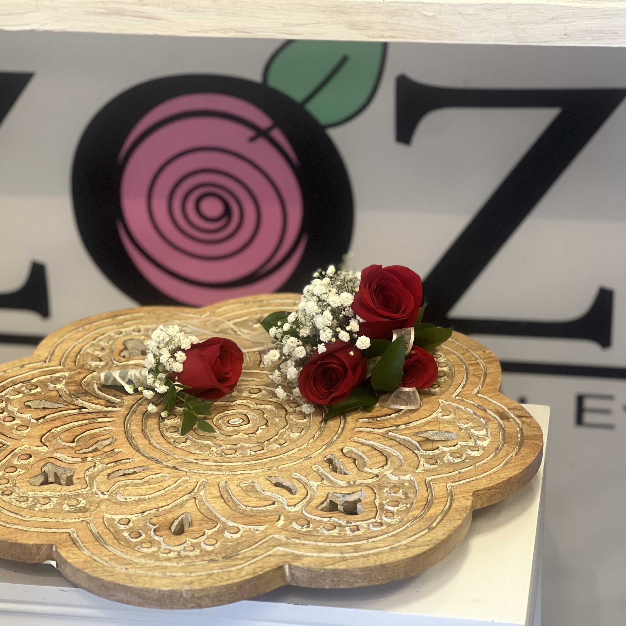 Two small red rose pieces with white filler flowers on a carved wooden stand