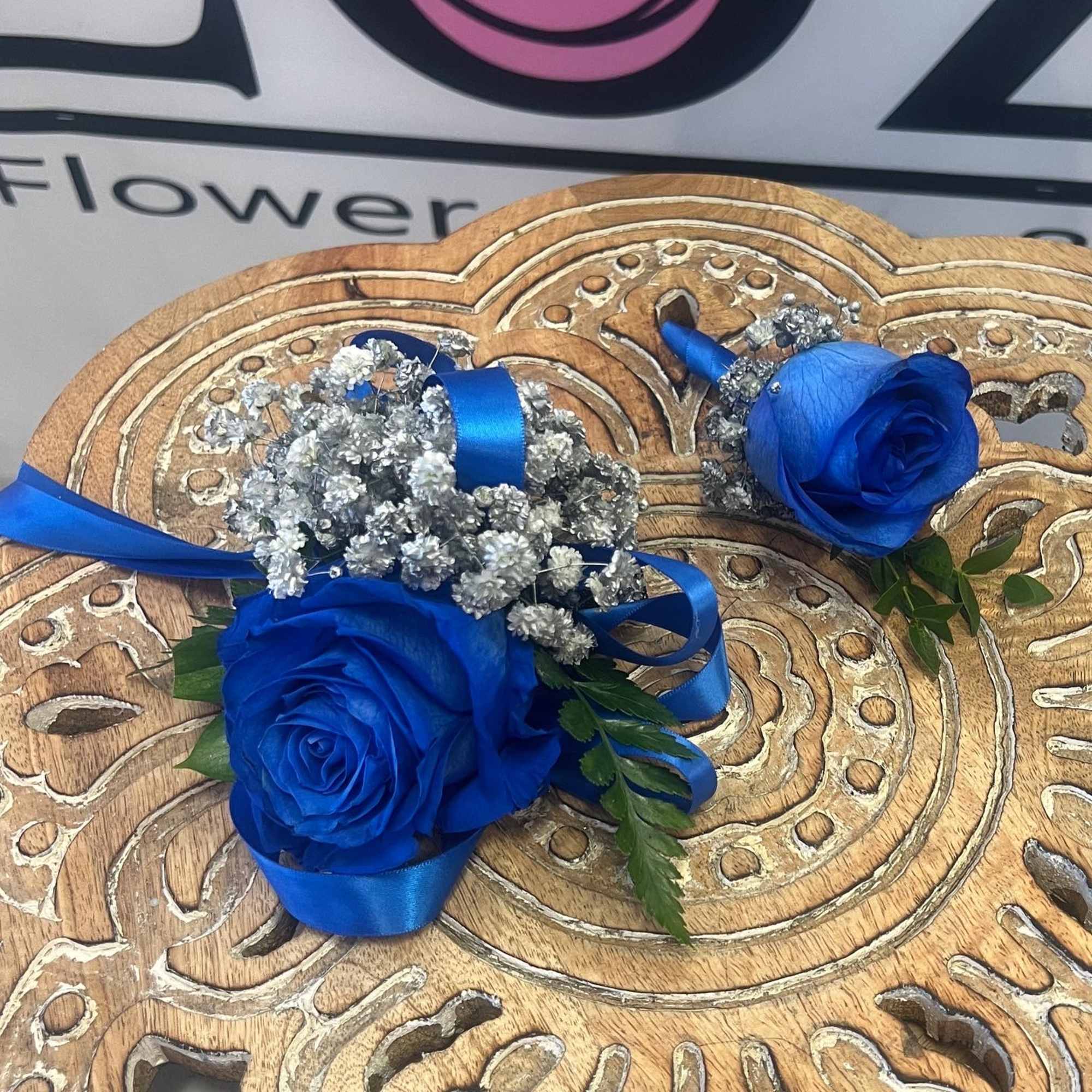 Two blue rose boutonnieres with silver baby's breath and ribbon
