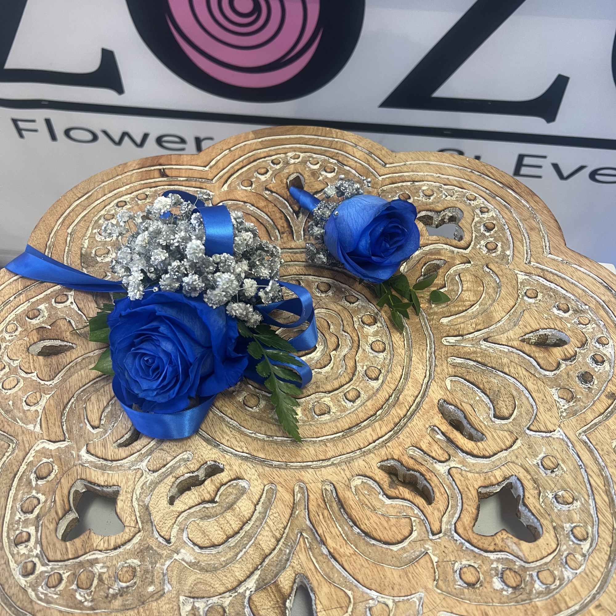 Two blue rose boutonnieres with silver filler and ribbon