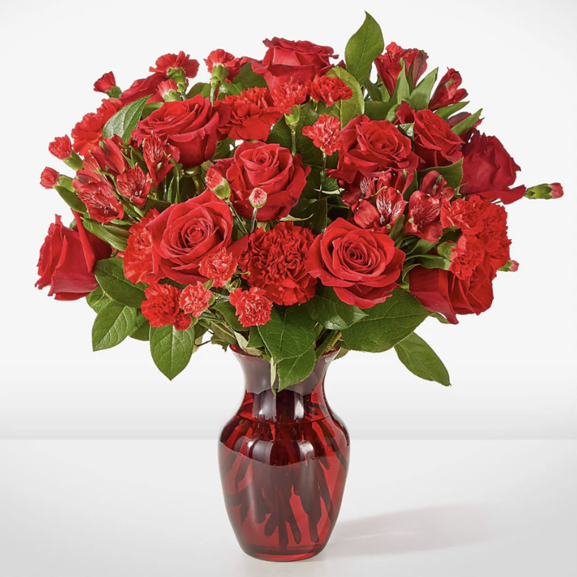 Red roses and carnations arranged in a red glass vase