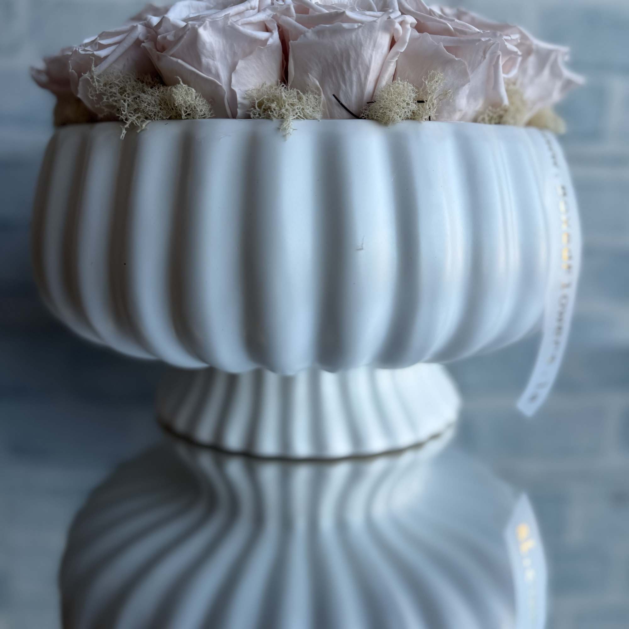 Pale pink roses arranged in a white pedestal vase