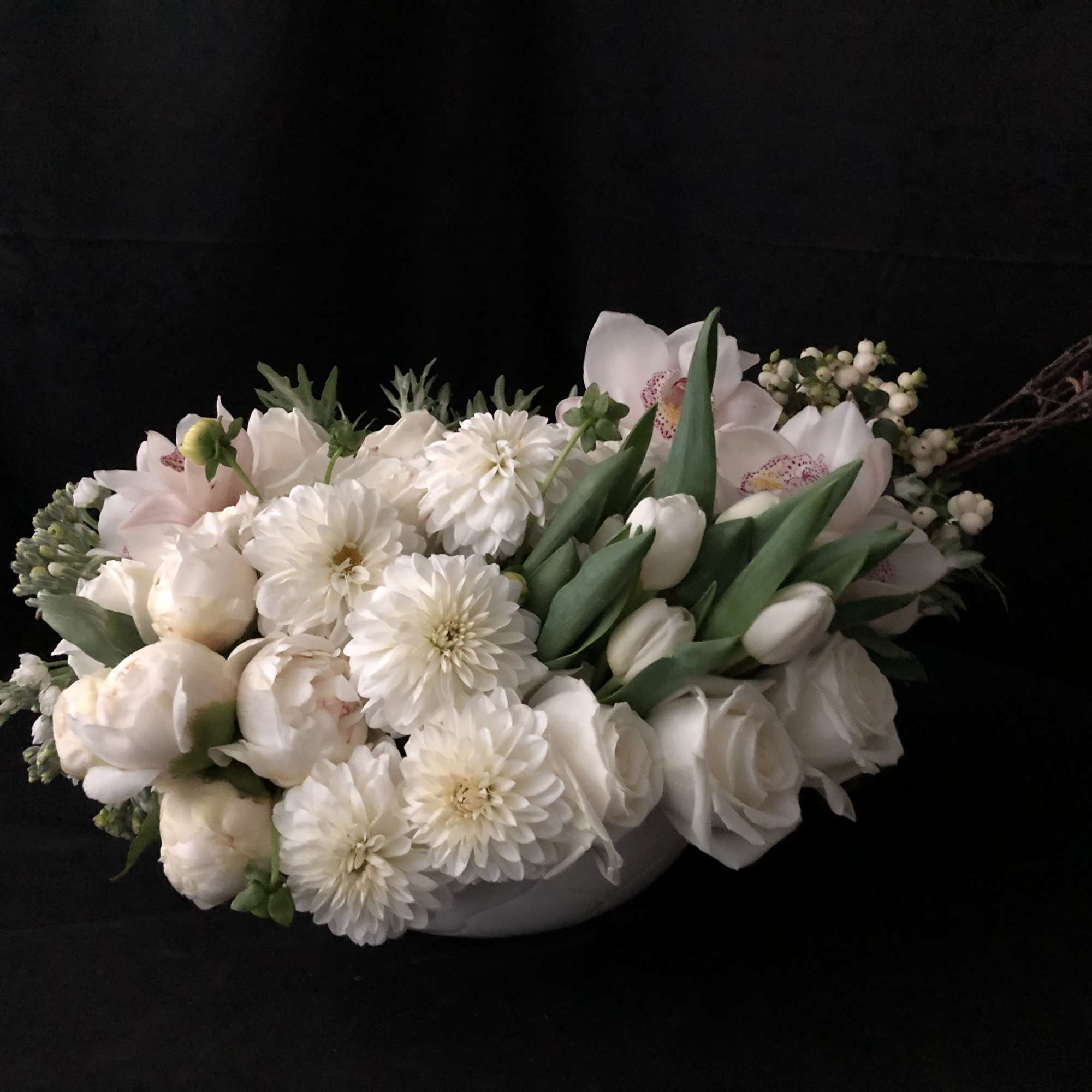 White floral arrangement with tulips, roses, and daisies in a low container