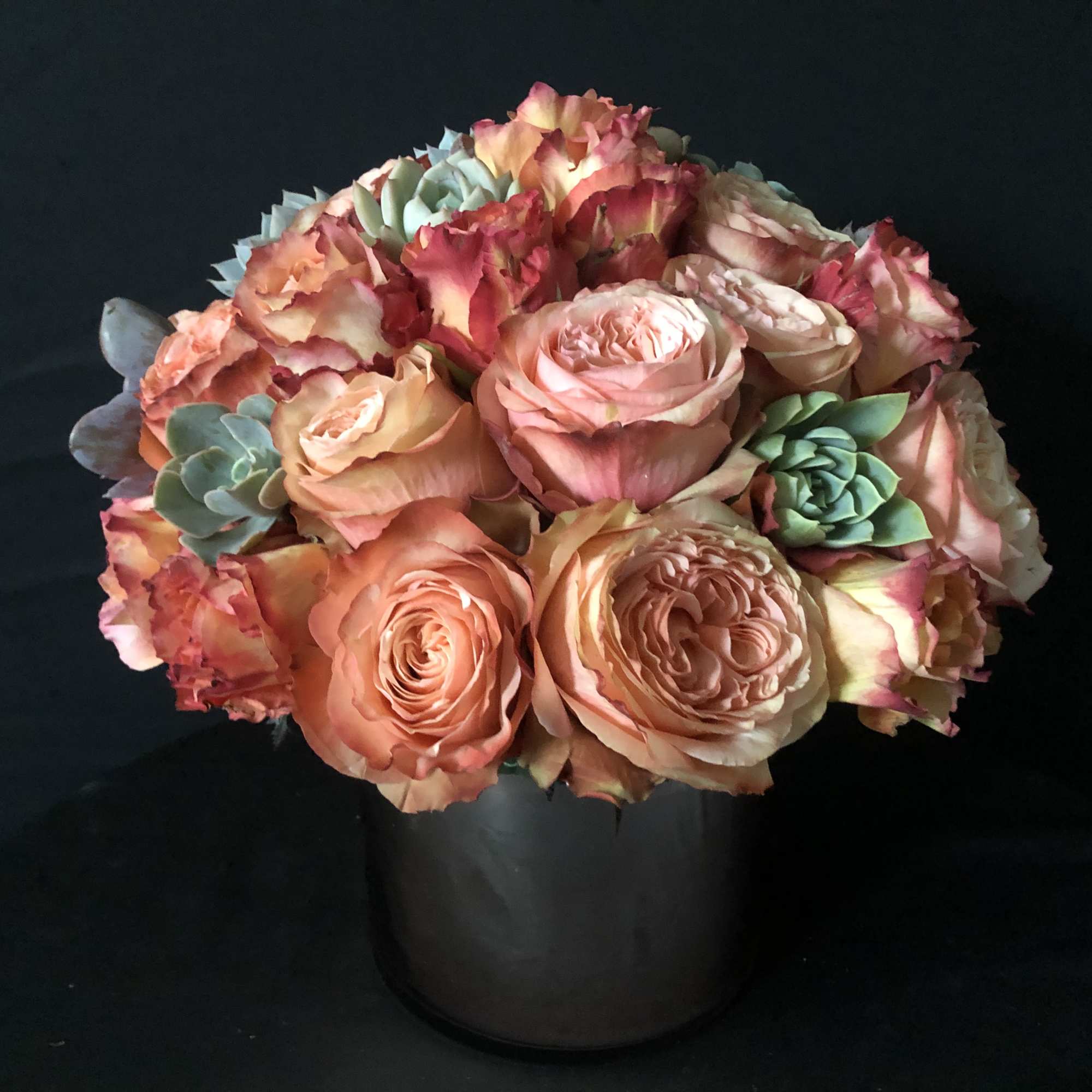 Peach and pink roses arranged in a black vase with small succulent accents