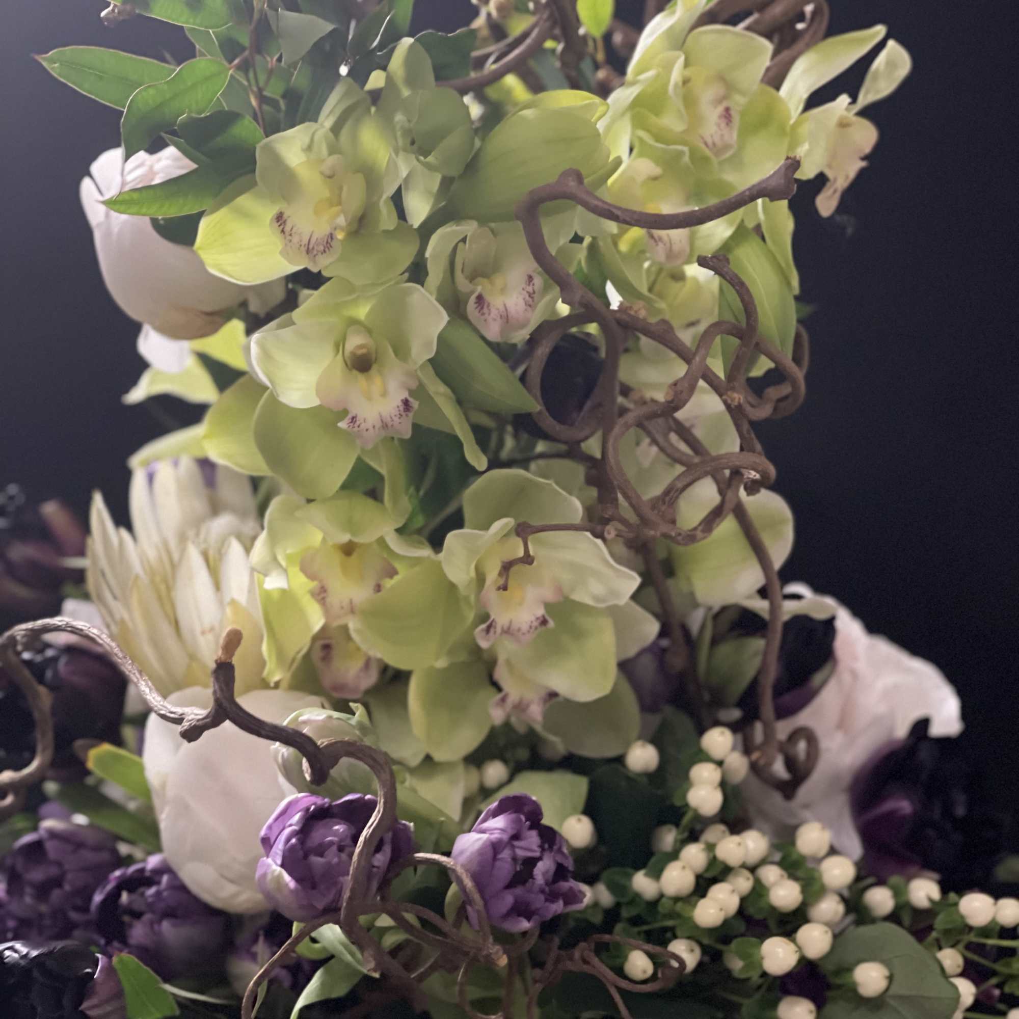 Tall floral arrangement with green orchids, purple blooms, and white berries