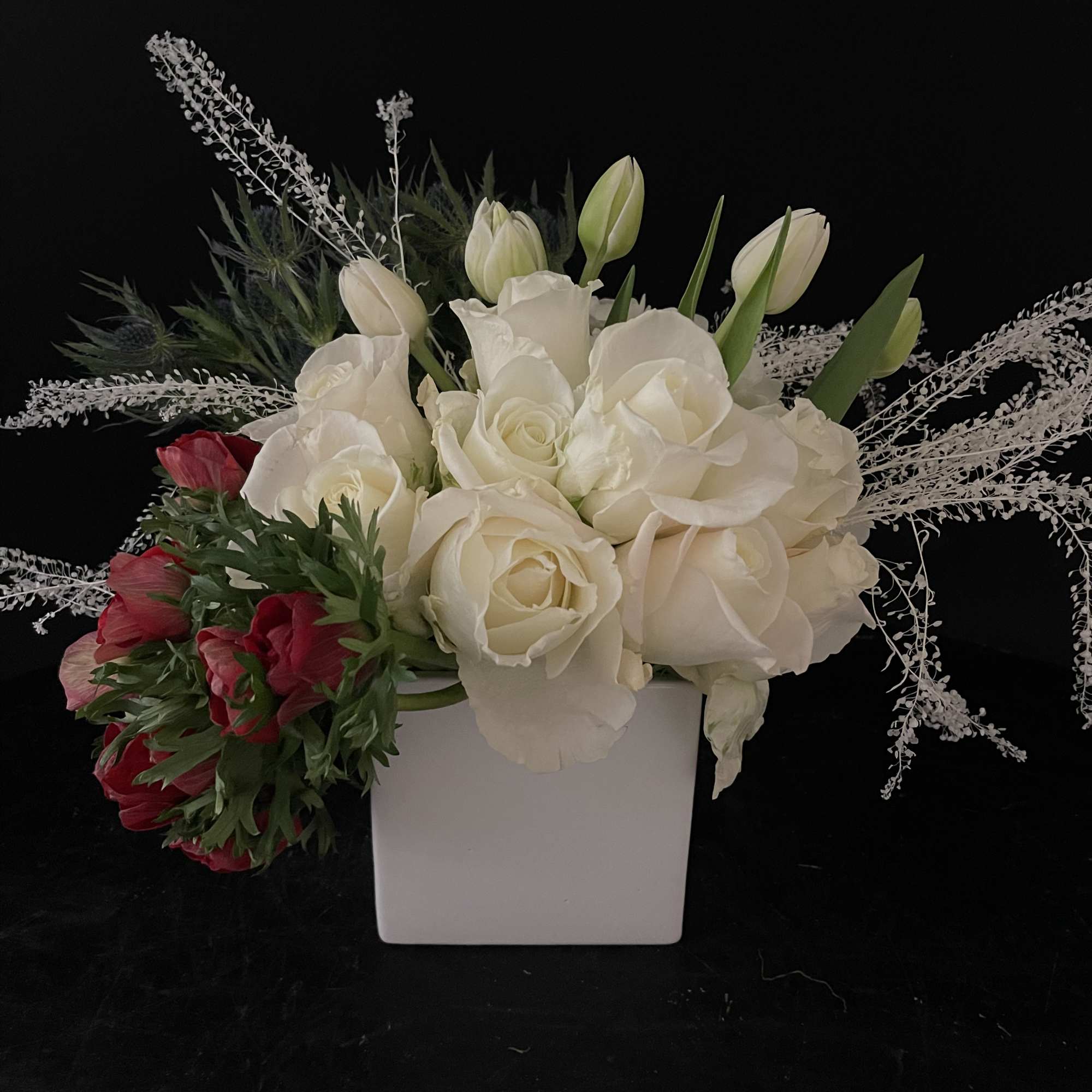 White roses and tulips in a white square vase with red blooms at one side