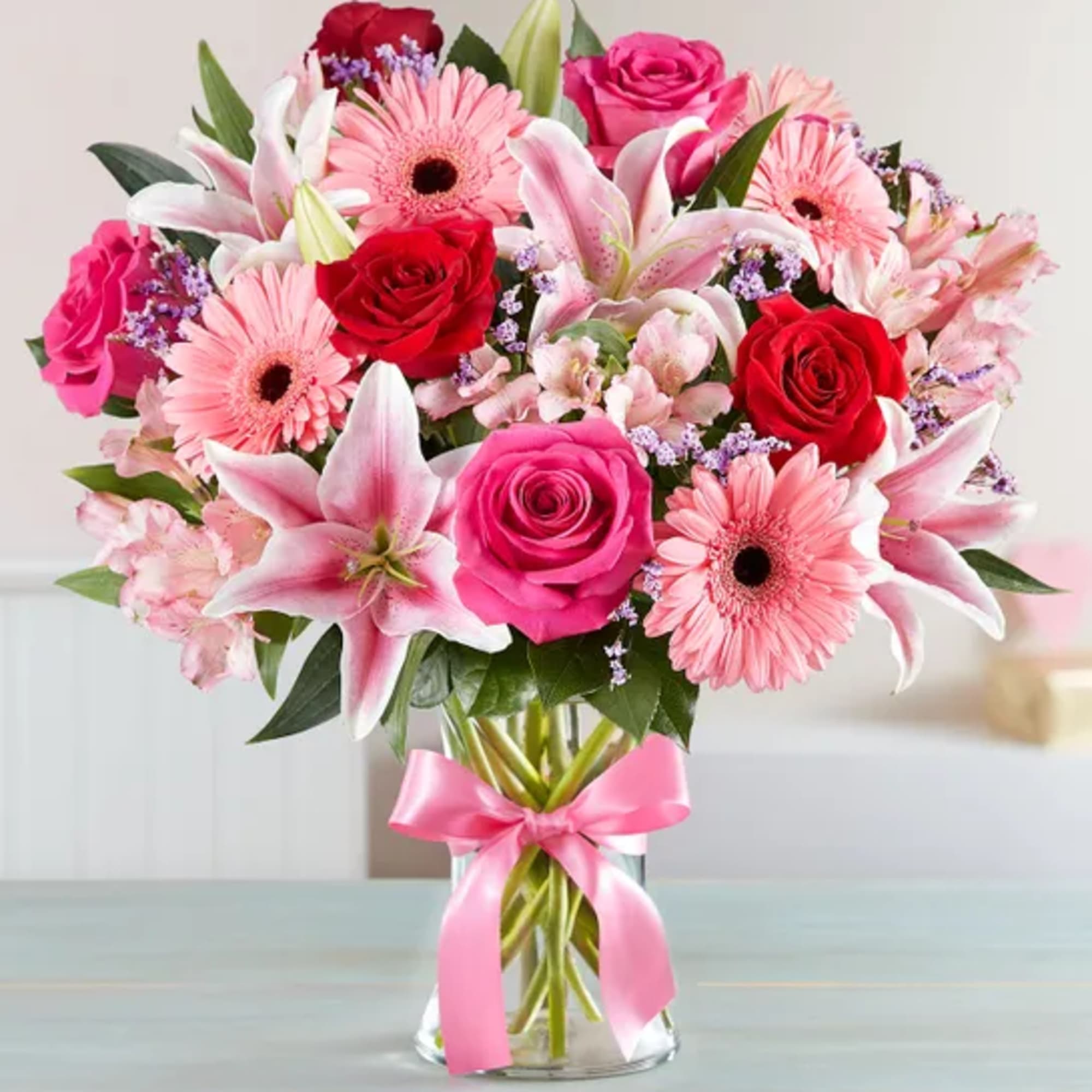 Pink and red bouquet of roses, lilies, and gerbera daisies in a glass vase