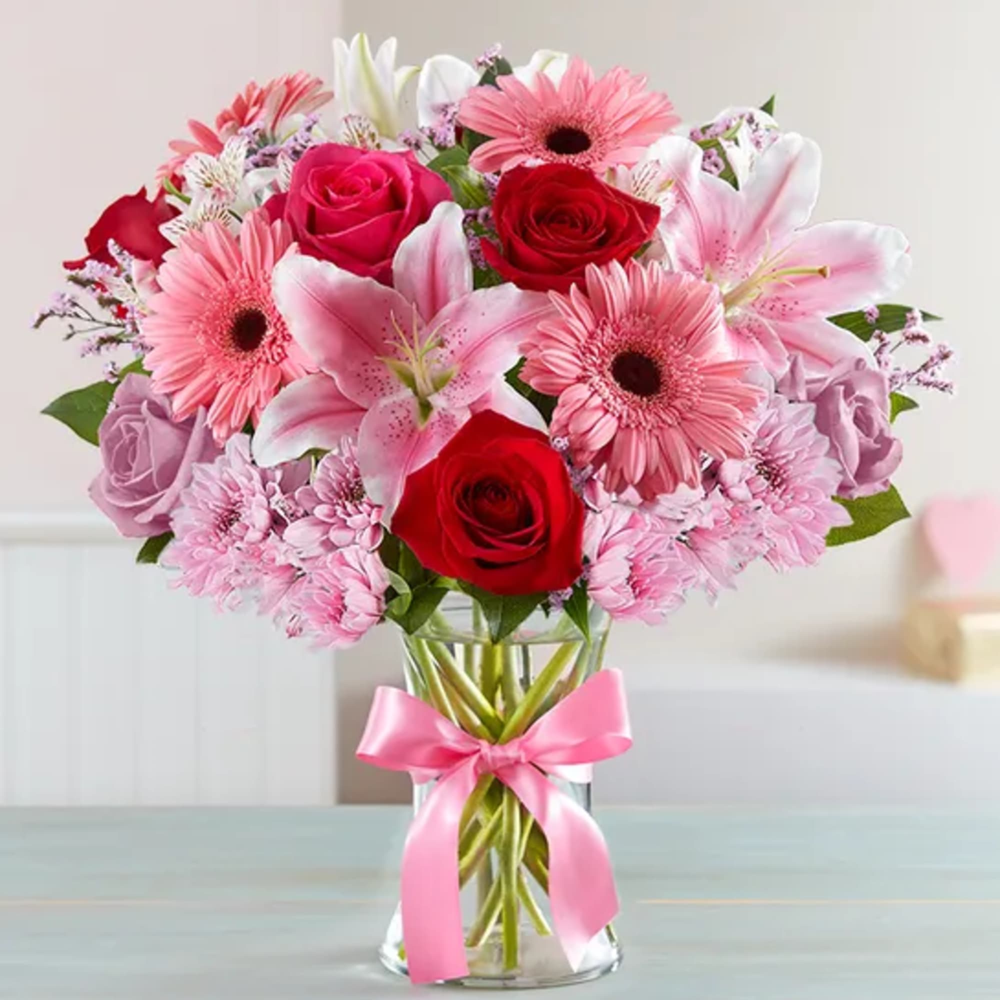 Pink and red mixed bouquet in a clear glass vase with a pink ribbon