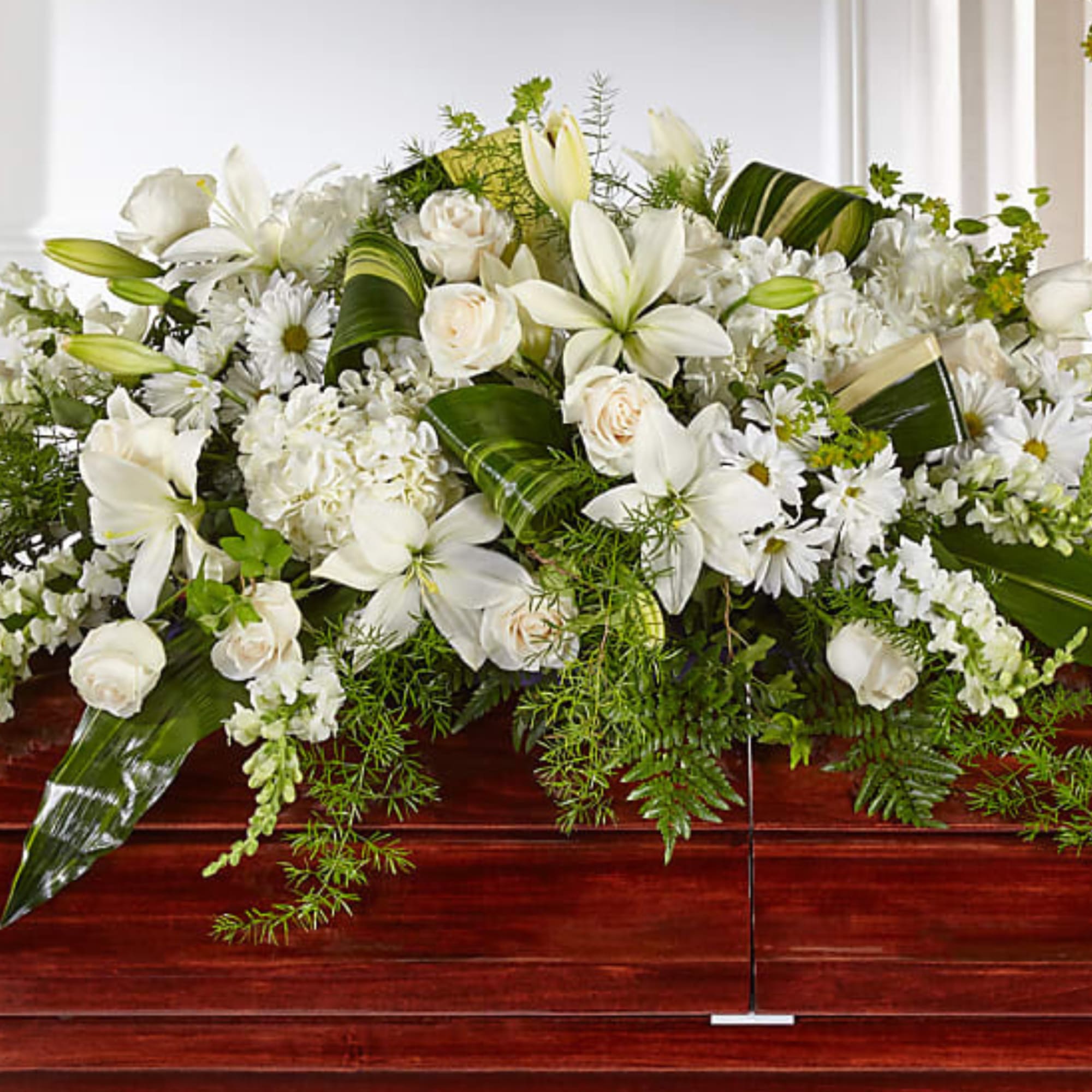White floral casket spray with lilies, roses, and daisies