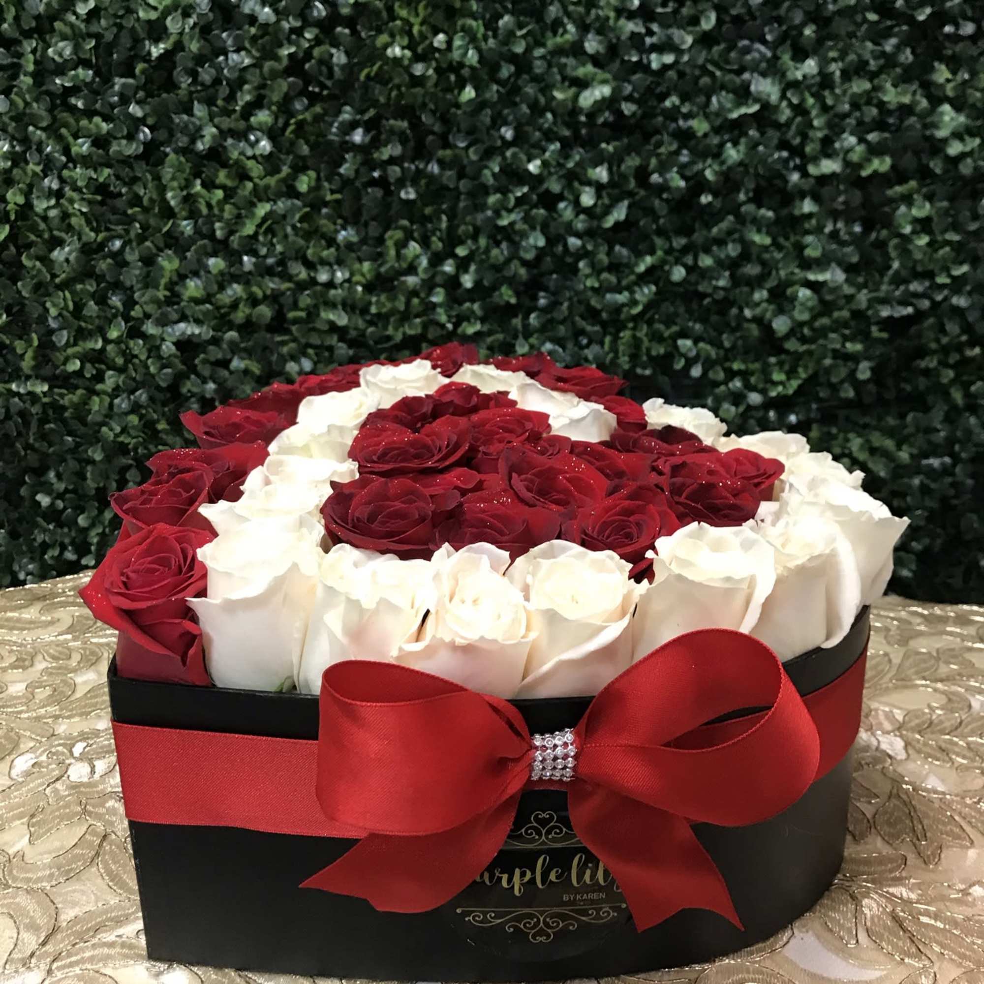 Red and white roses arranged in a black box with a red ribbon bow