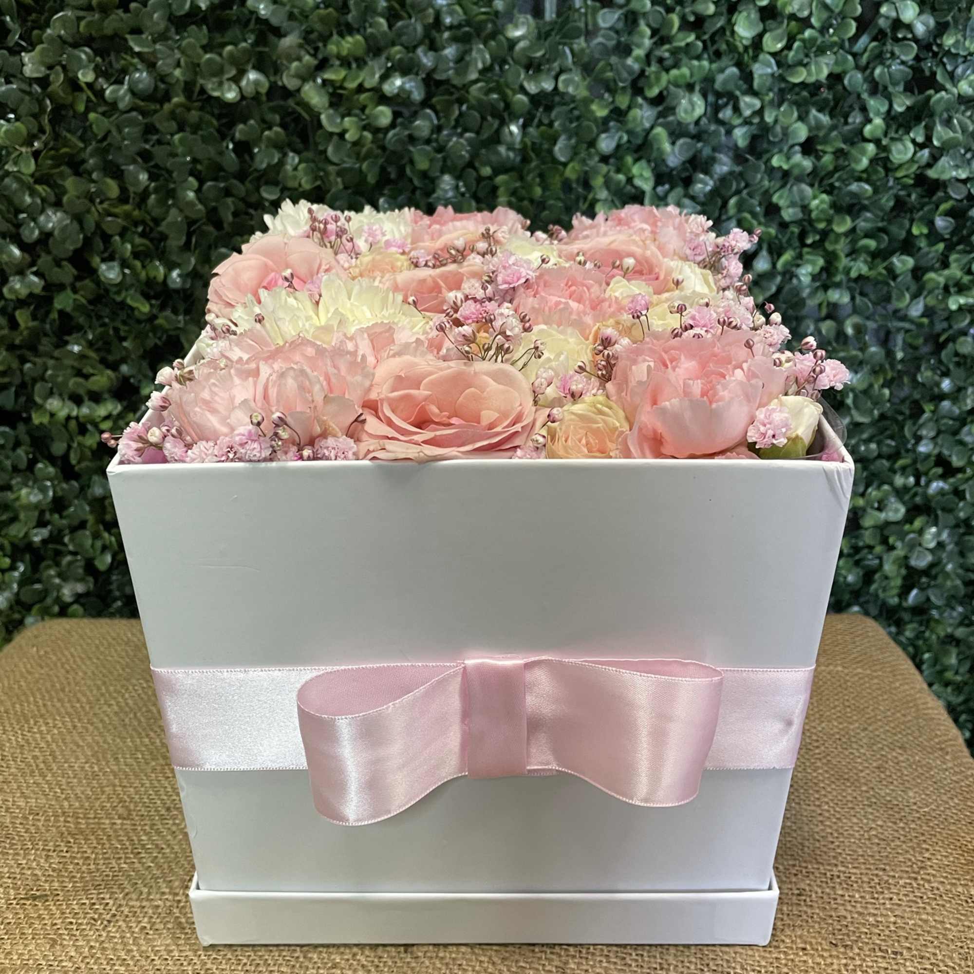 Pink and cream flowers arranged in a white box with a pink ribbon