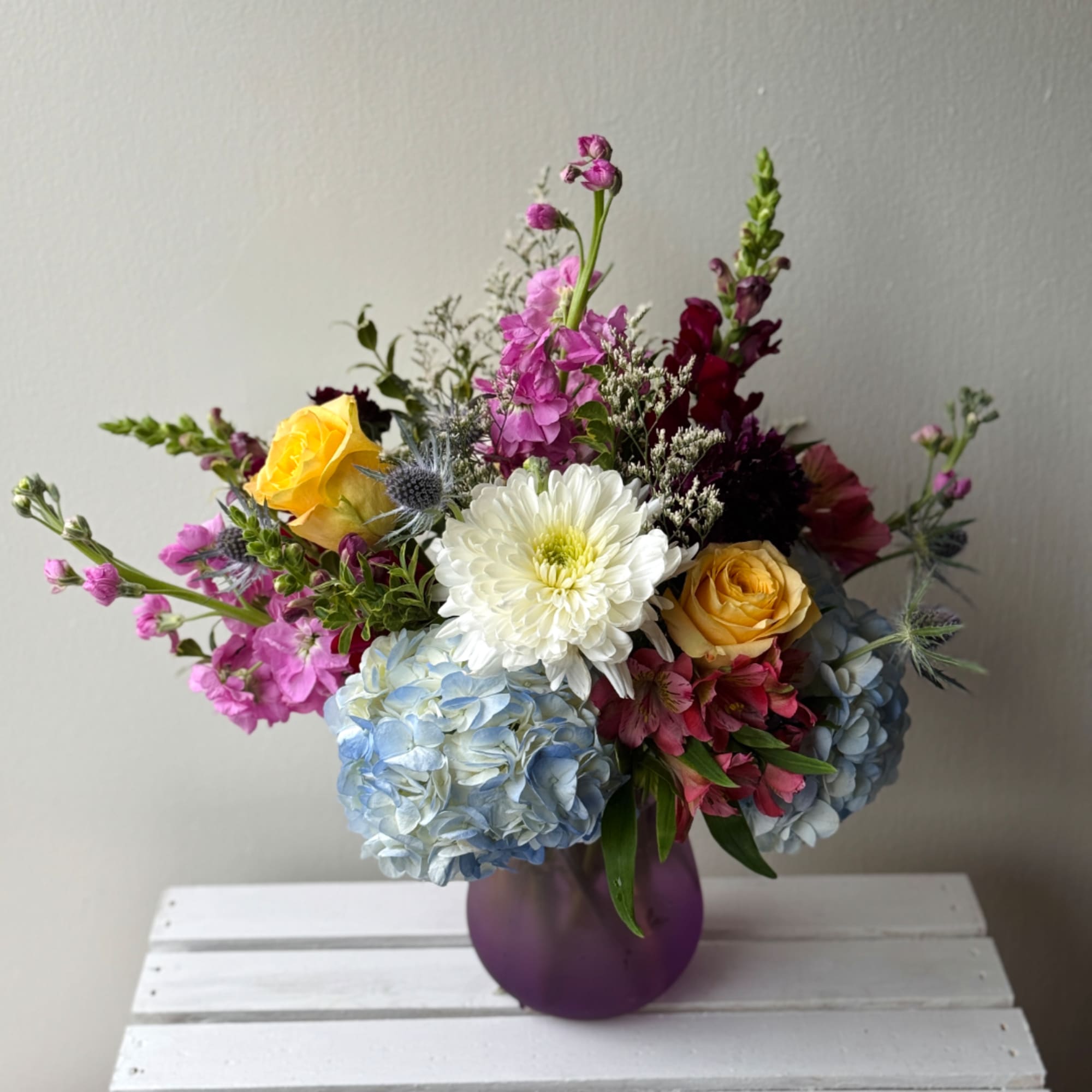Mixed bouquet in a purple vase with roses, hydrangeas, and a white chrysanthemum