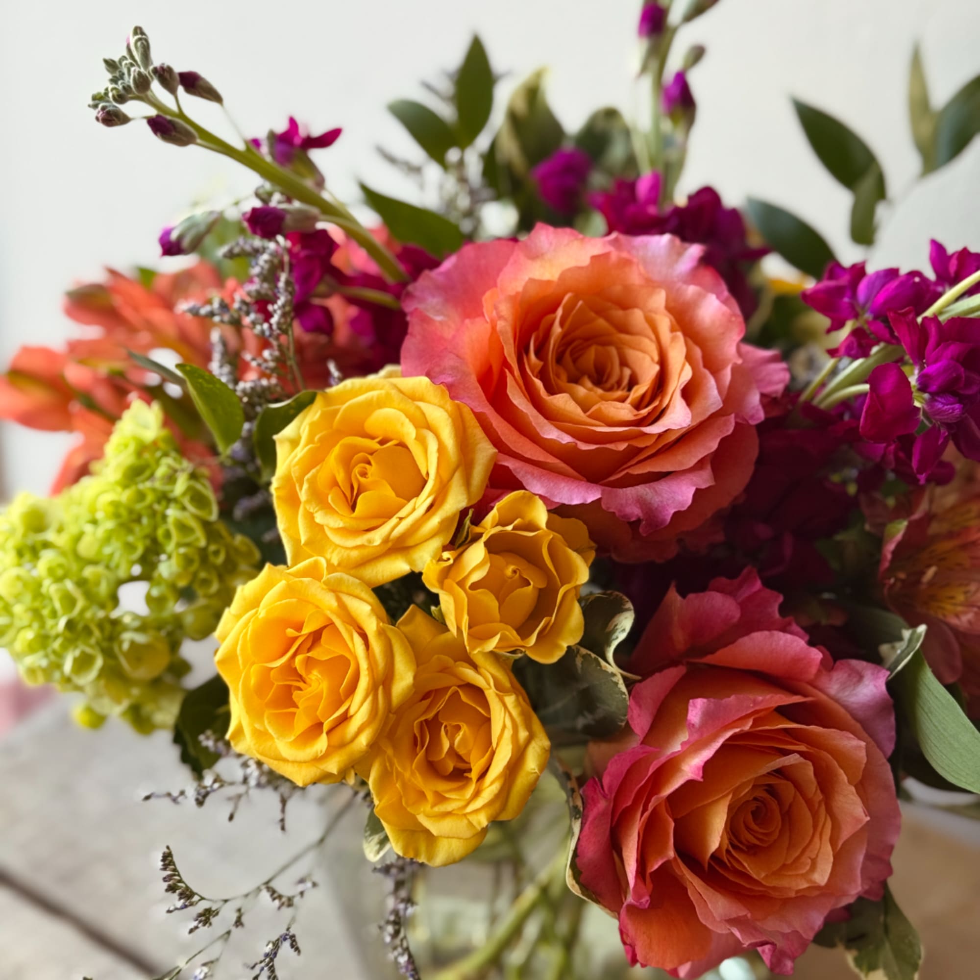 Bouquet of orange and yellow roses with purple flowers in a glass vase