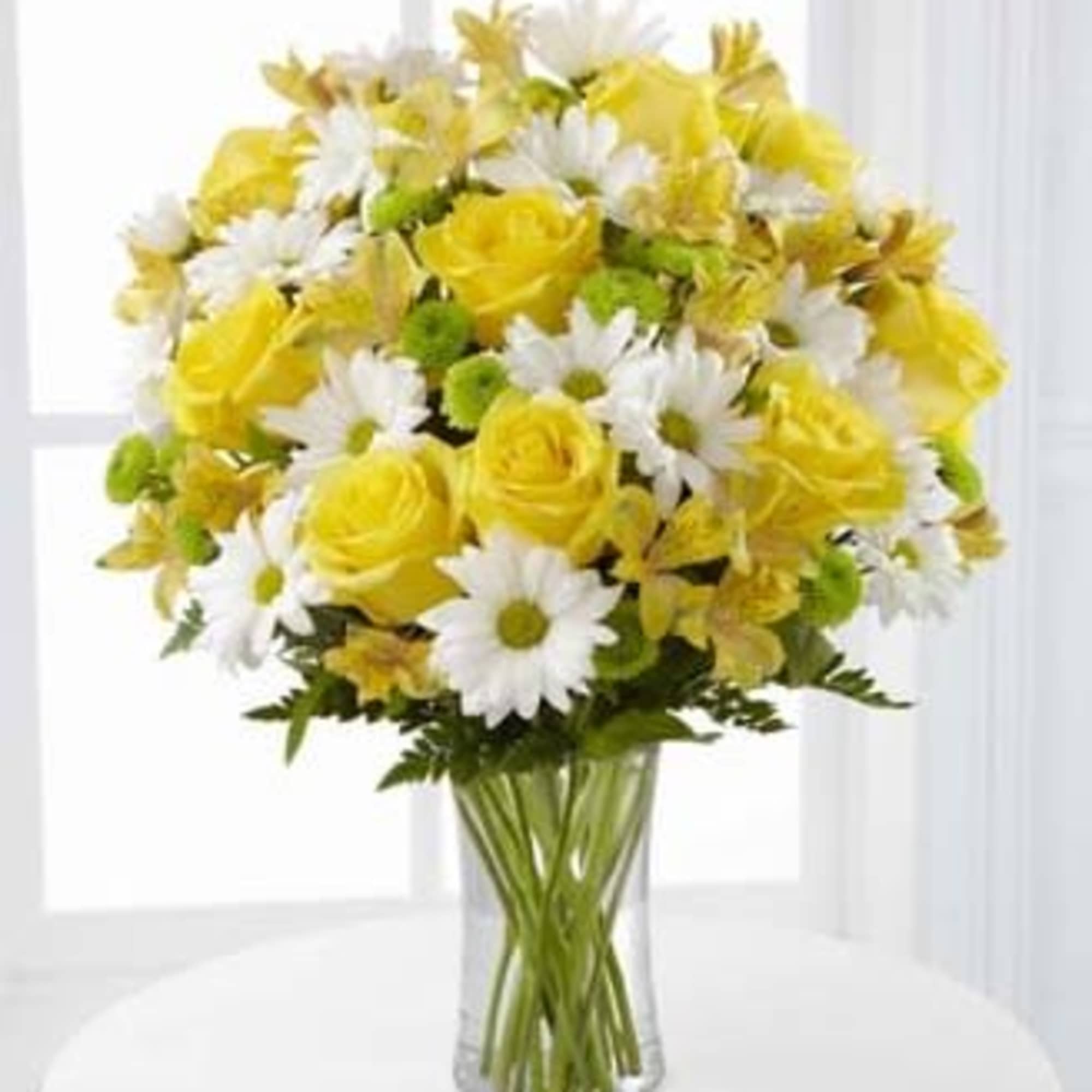 Bouquet of yellow roses, white daisies, and green button poms in a clear glass vase