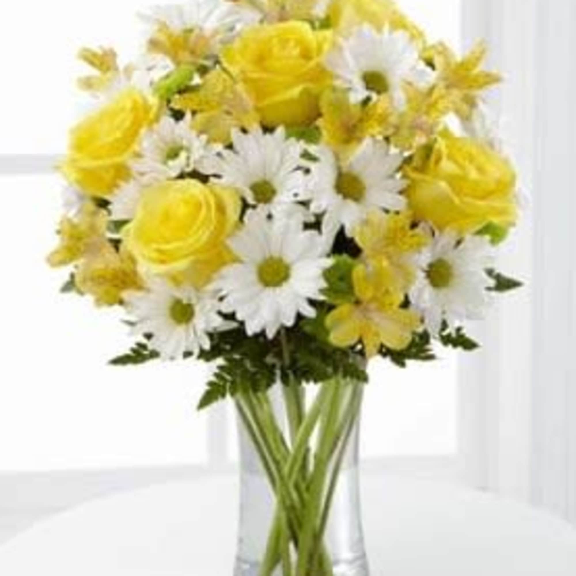 Arrangement of yellow roses, white daisies, and yellow blooms in a clear glass vase