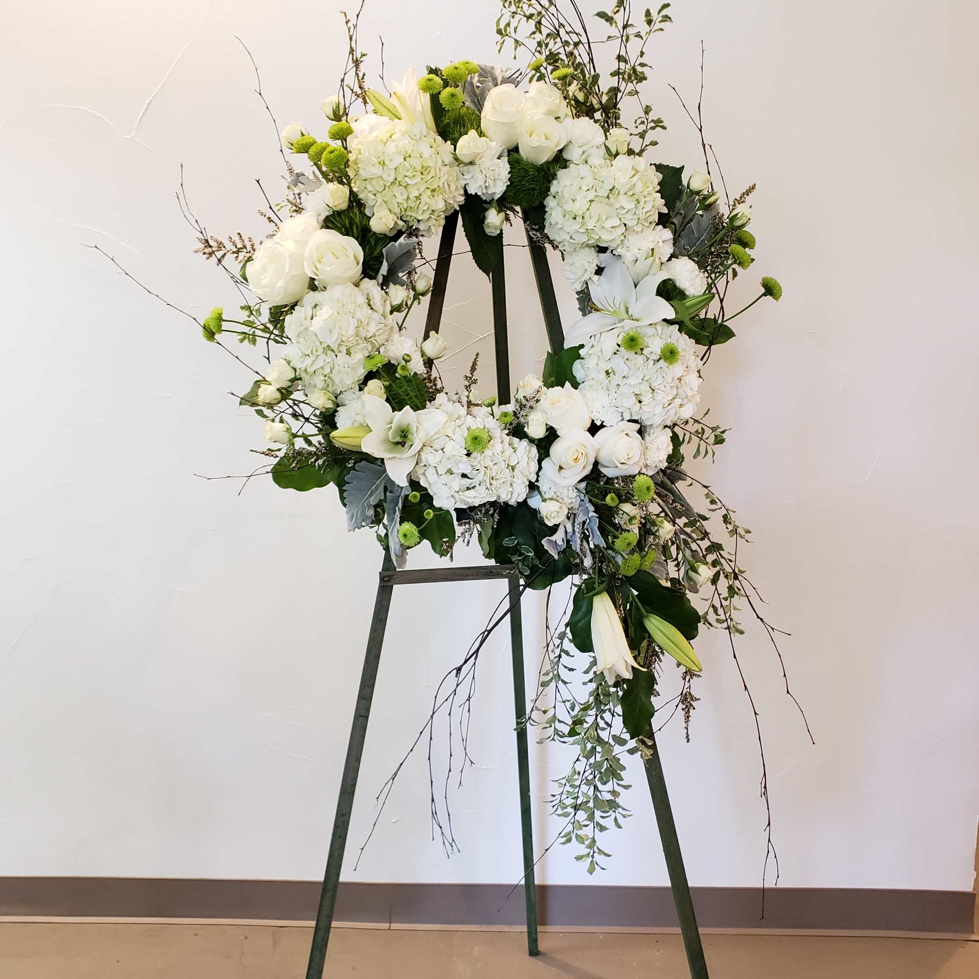 White floral wreath on a standing easel with trailing branches
