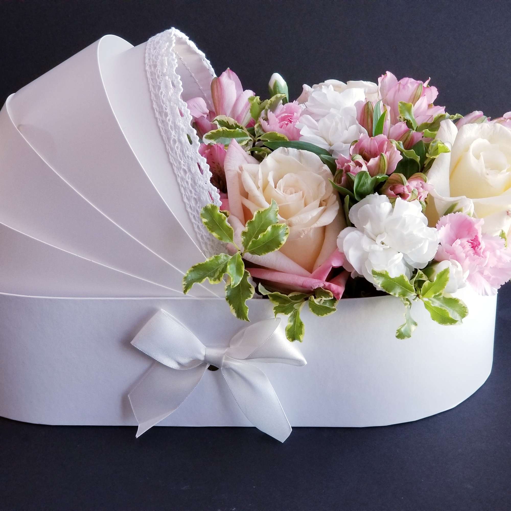 Pink and white roses arranged in a white heart-shaped box