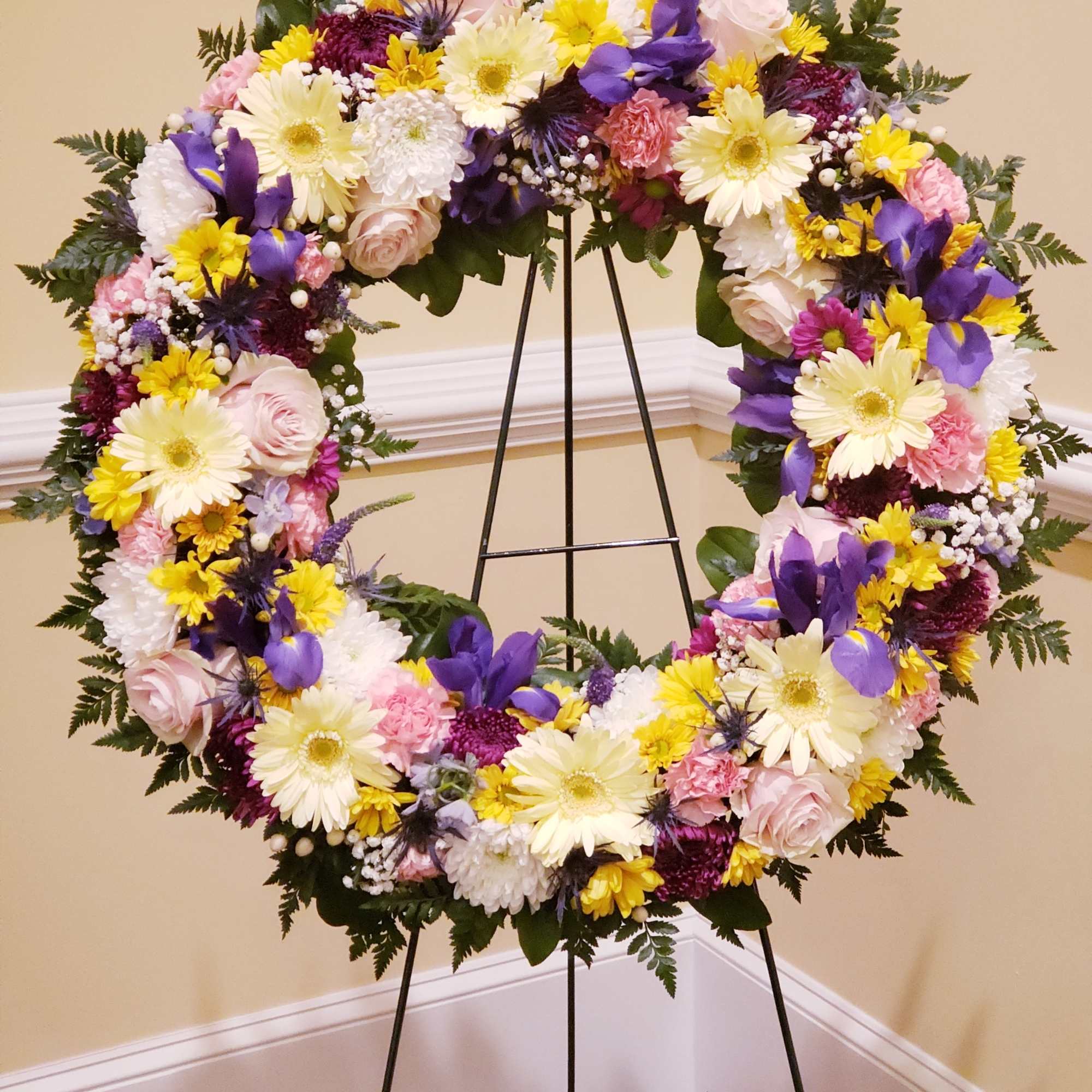 A bright standing wreath of greenery and fresh flowers in yellow, pink