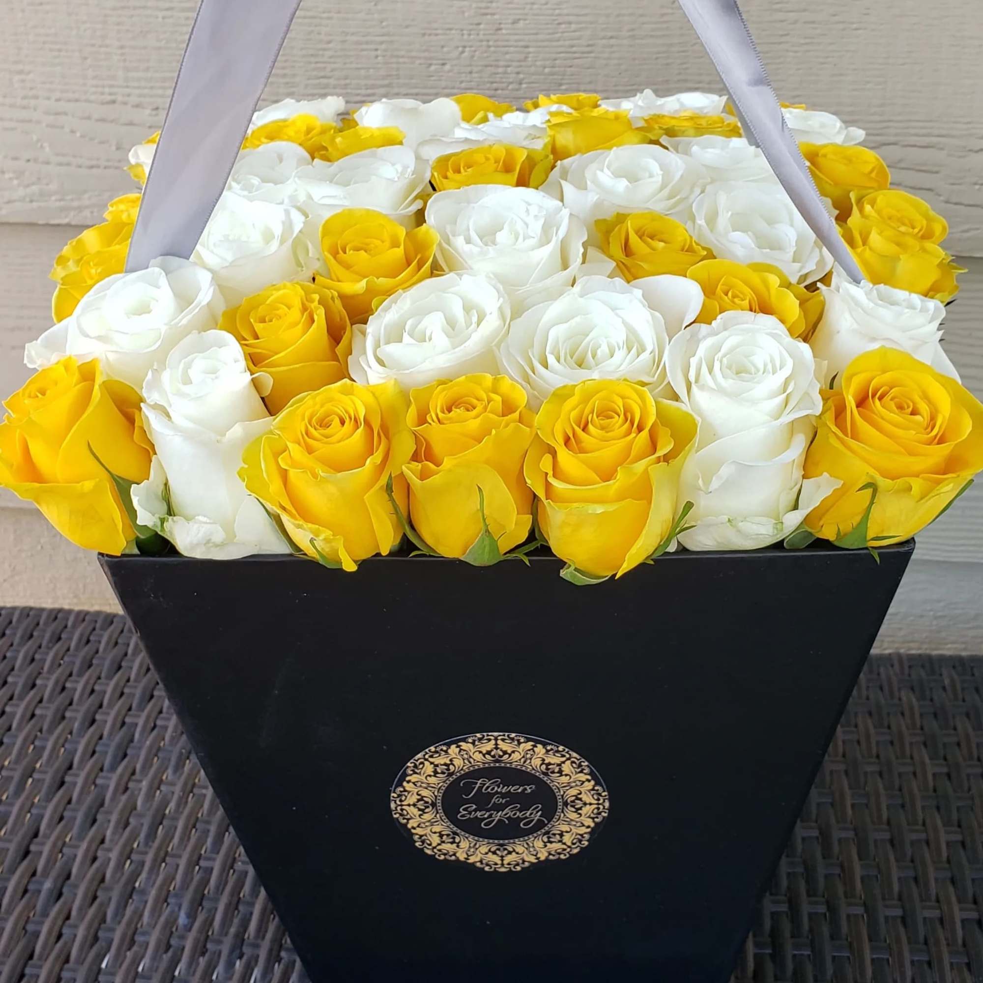 Yellow and white roses arranged in a black gift box with ribbon handles