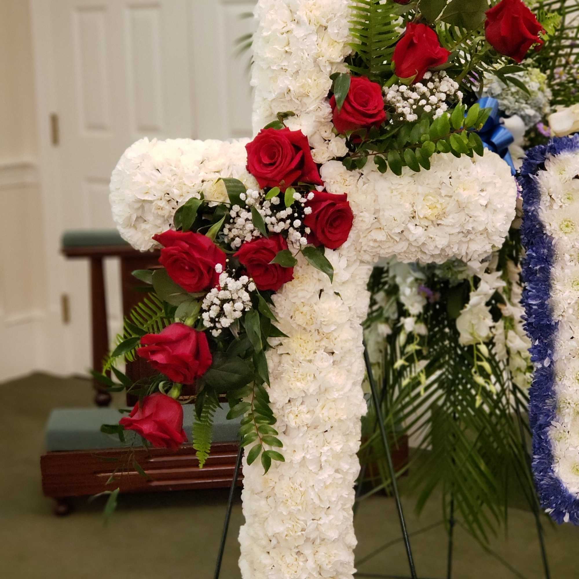Standing spray cross of white blossoms (carnations) adorned with red roses. It&rsquo;s, photo 2 of 2
