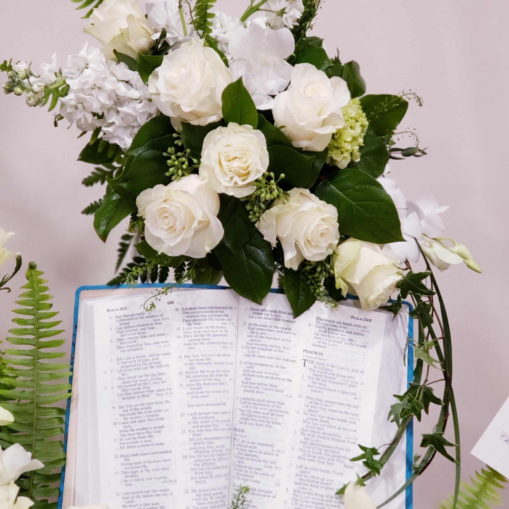 White rose arrangement above an open Bible with greenery